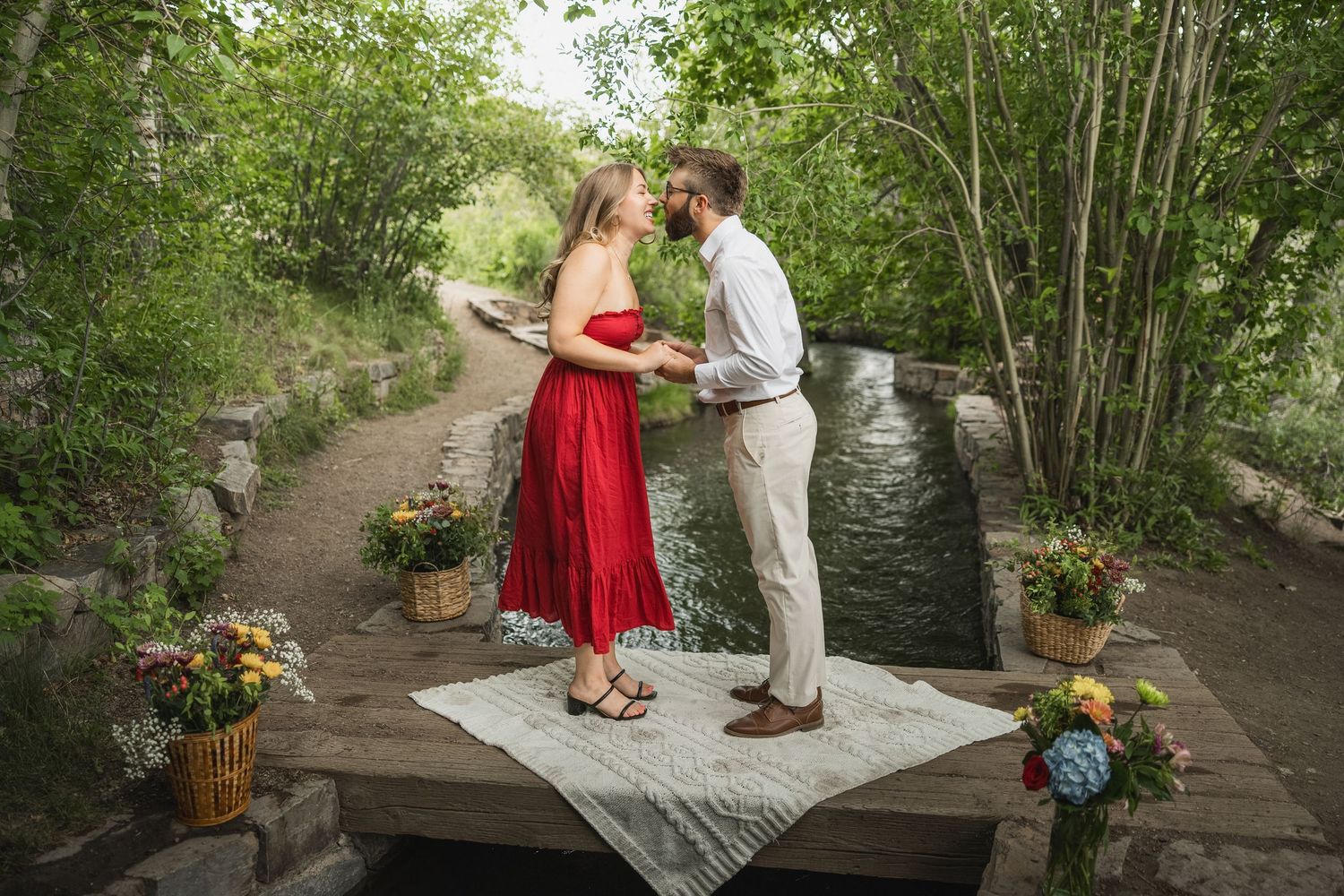 Two people share a tender moment on a stone platform decorated with colorful flower arrangements.
