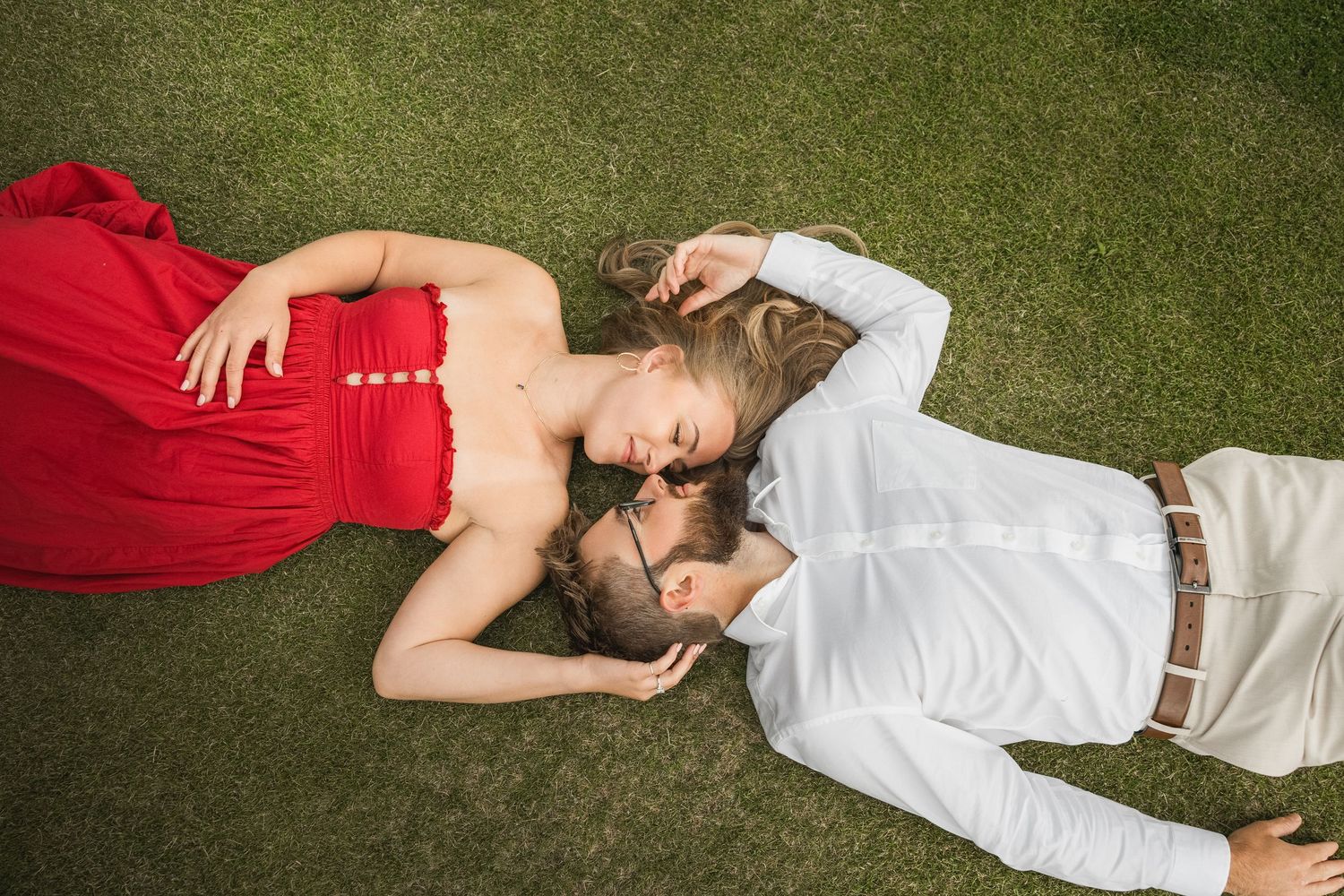 A couple in red and white summer outfits lying on green grass together.