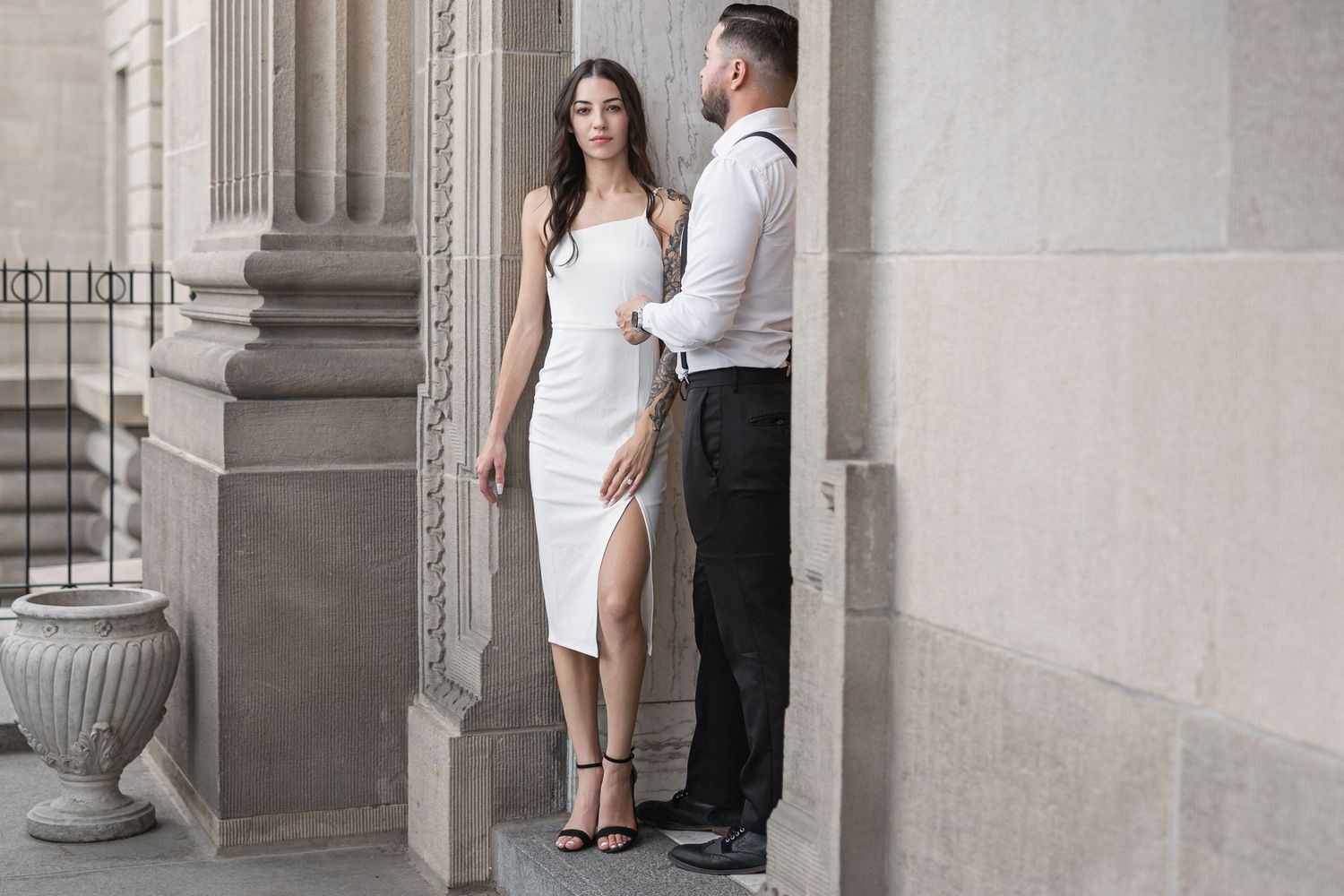 Romantic couple shares intimate moments against a classic stone building backdrop.