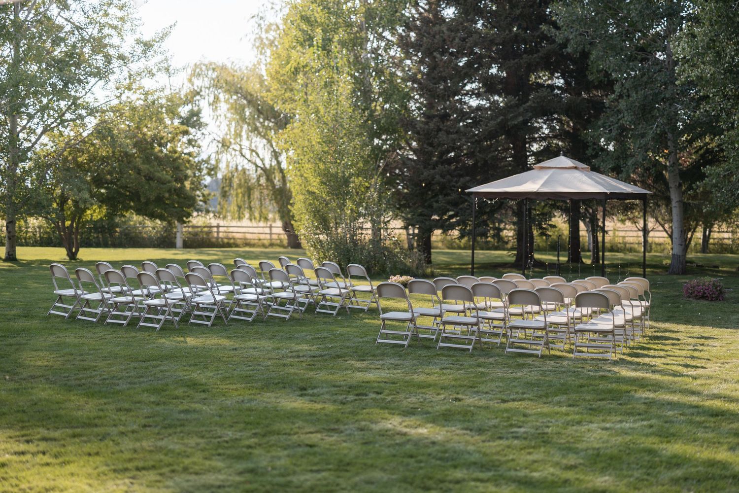 White folding chairs arranged in neat rows on a sunlit lawn for an outdoor wedding ceremony.