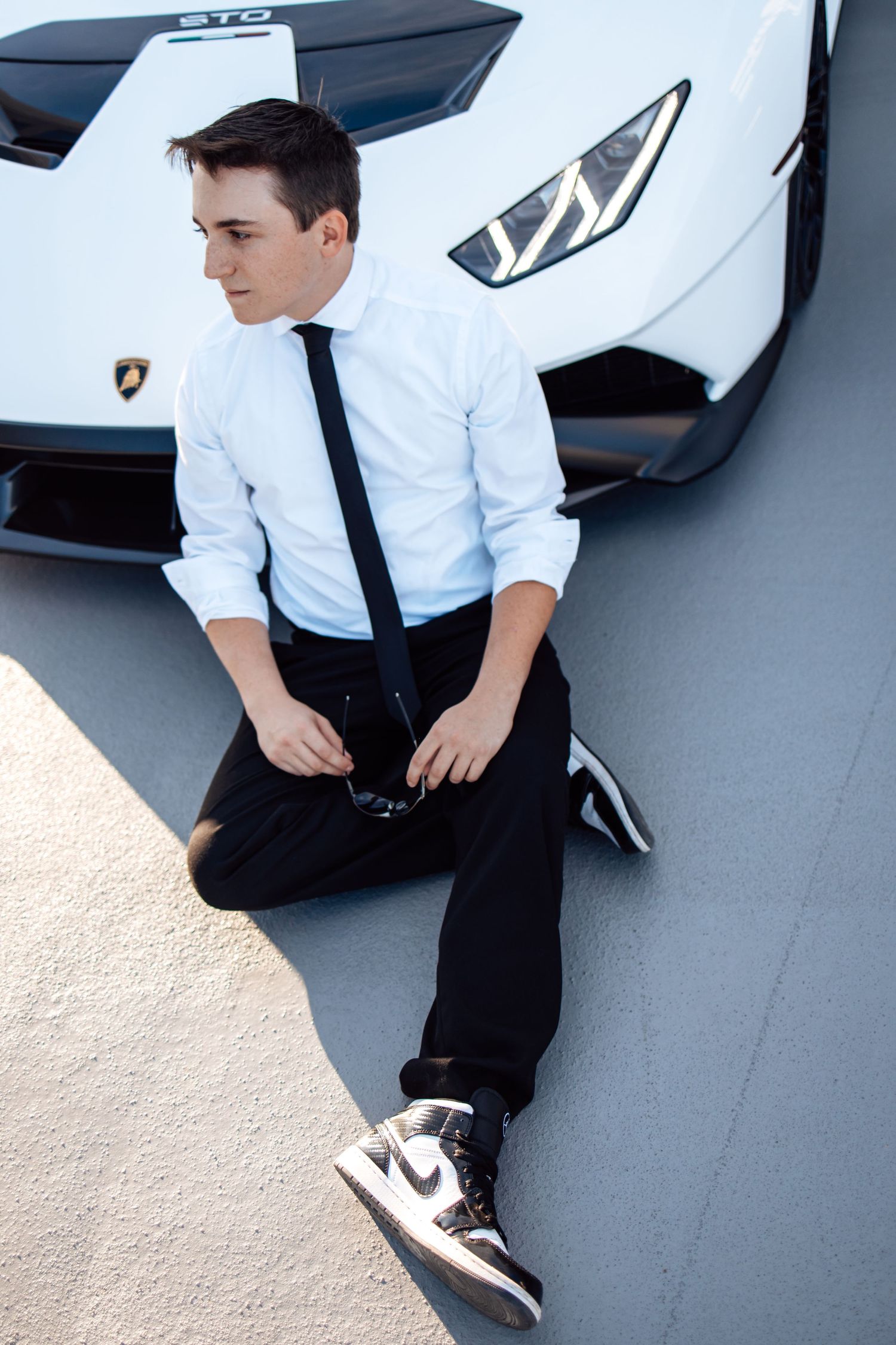 Person in formal attire sitting on hood of white Lamborghini supercar.