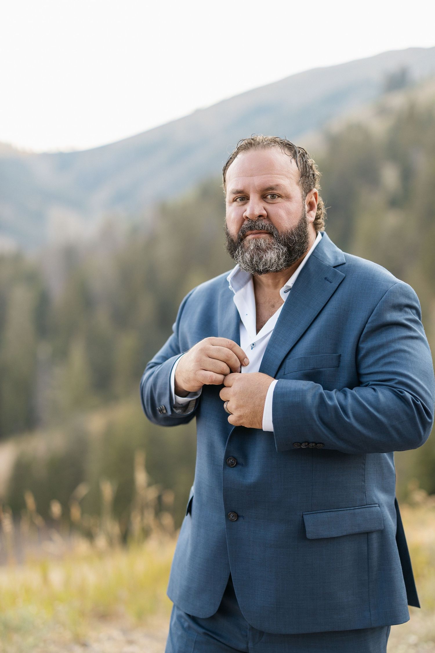 Person in blue suit making expressive gestures against mountain backdrop.