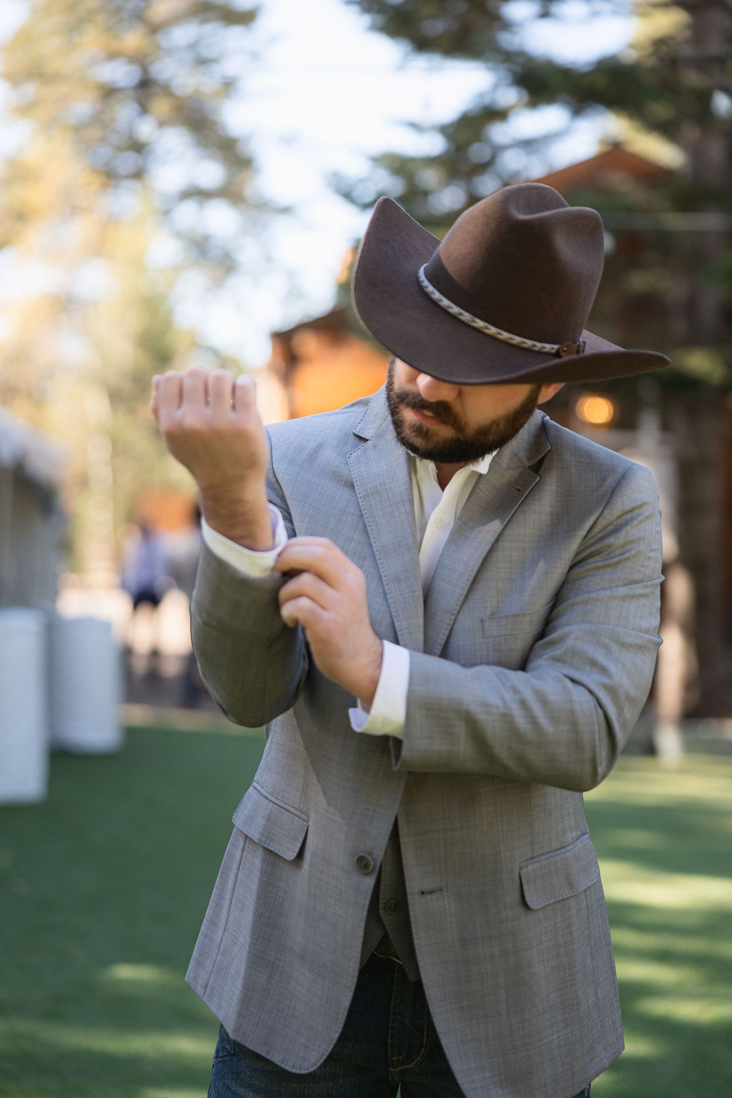 Person in grey suit and cowboy hat striking fun poses against outdoor backdrop.