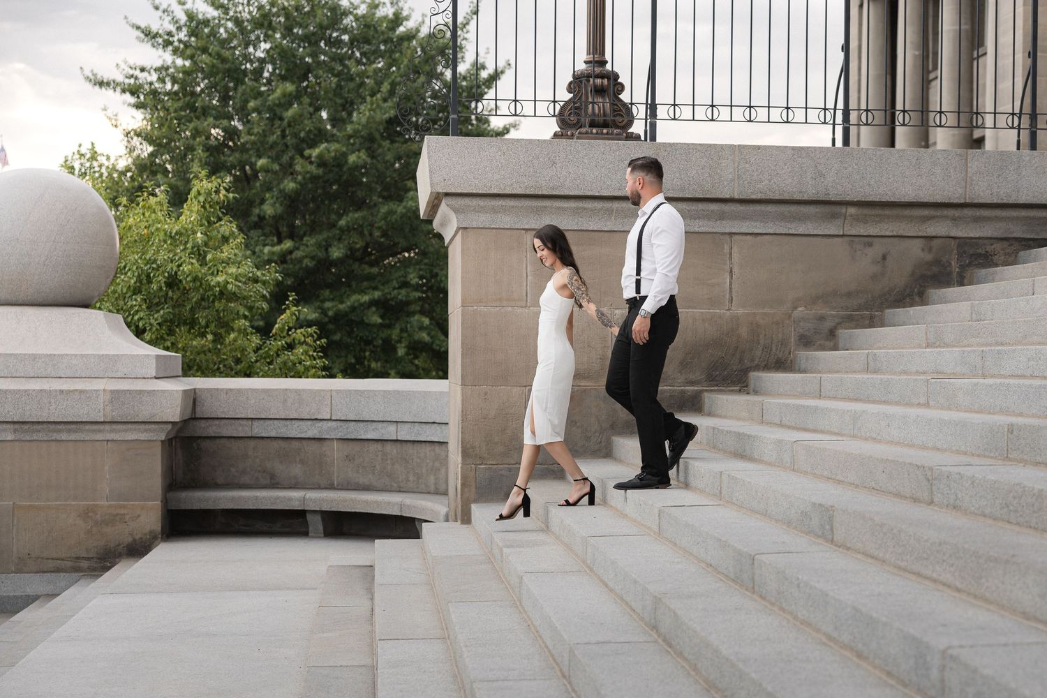 A couple in formal attire walking up elegant stone stairs at a grand building entrance.