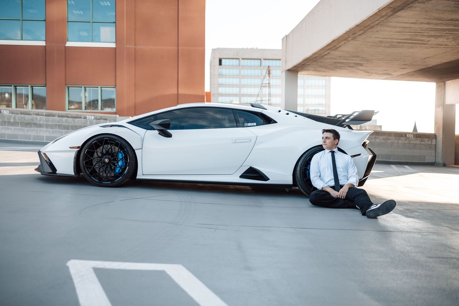 A white Lamborghini supercar parked in a modern parking structure with glass and concrete architecture.