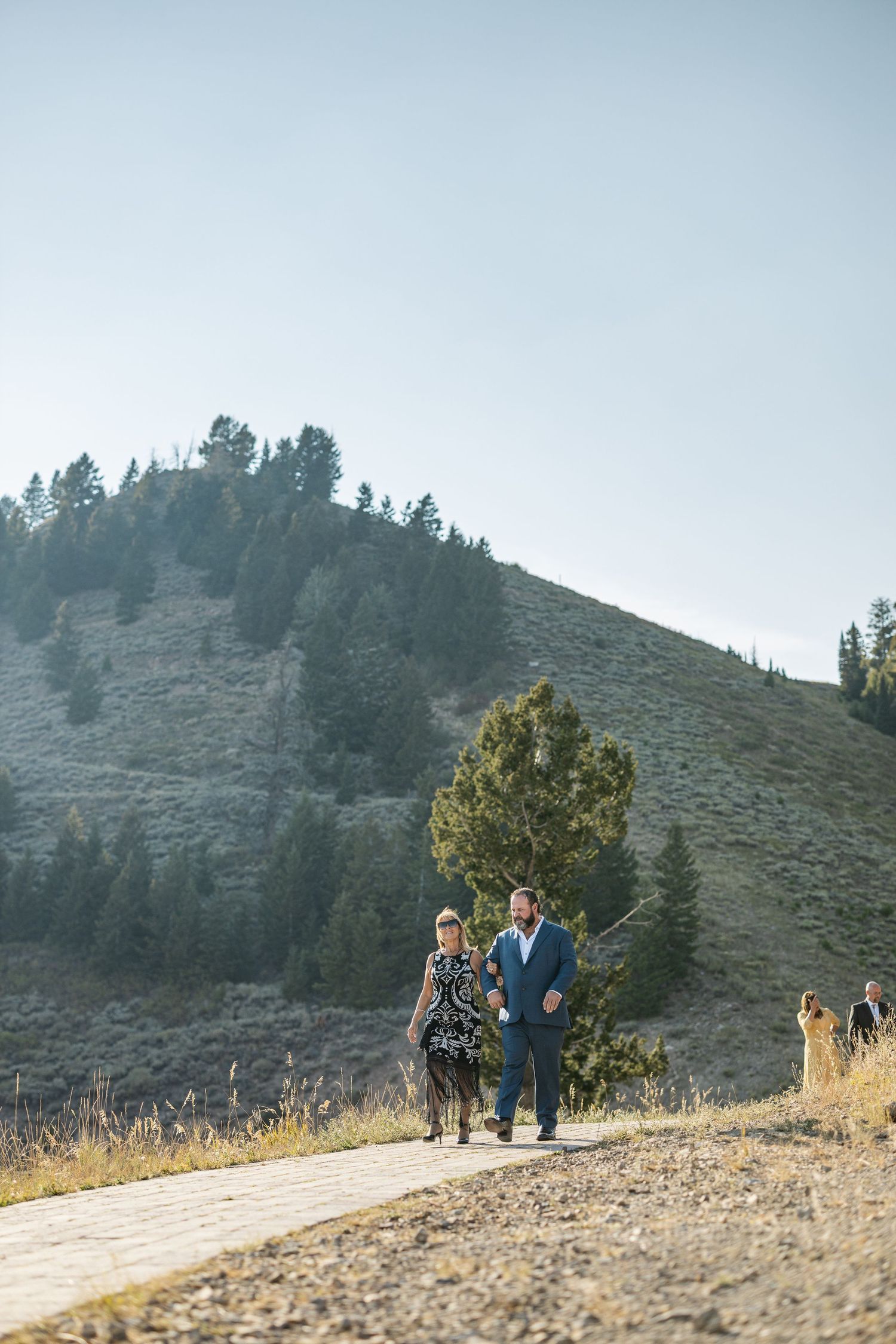 Couple walking along mountain path during golden hour.