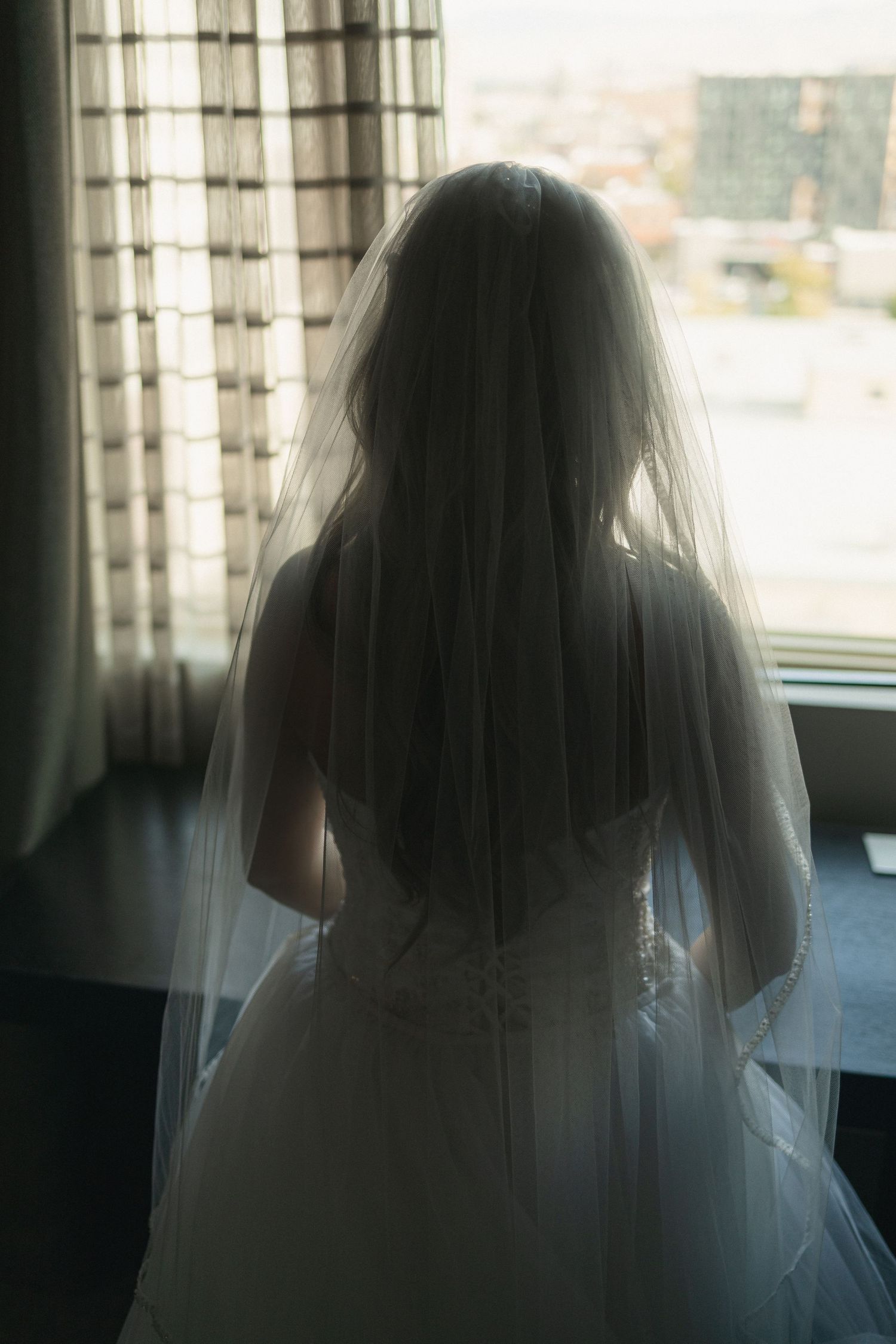 Silhouette of bride in wedding dress looking out window.