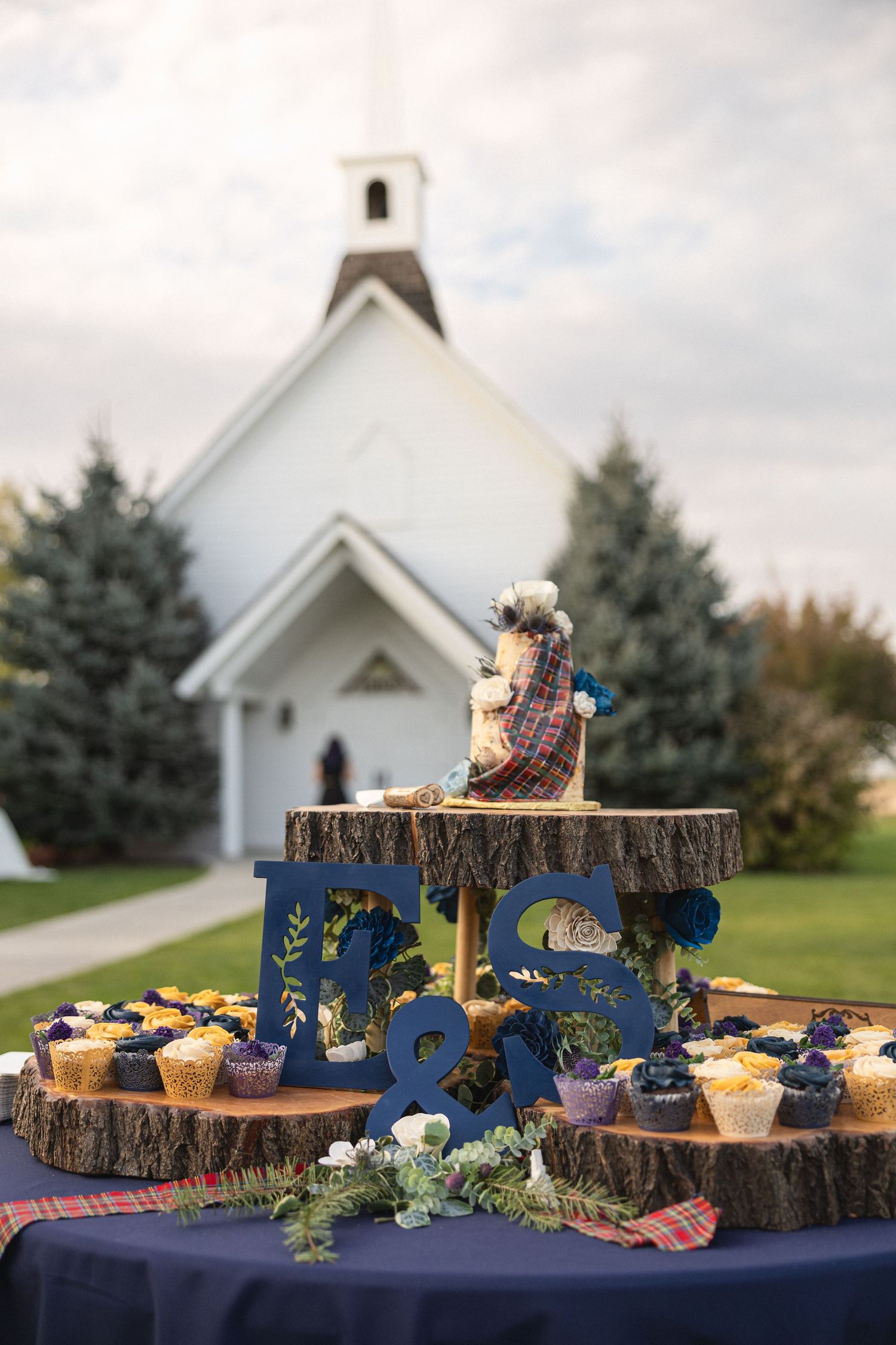 Rustic wedding cupcake display on wood slices with a white chapel in the background.