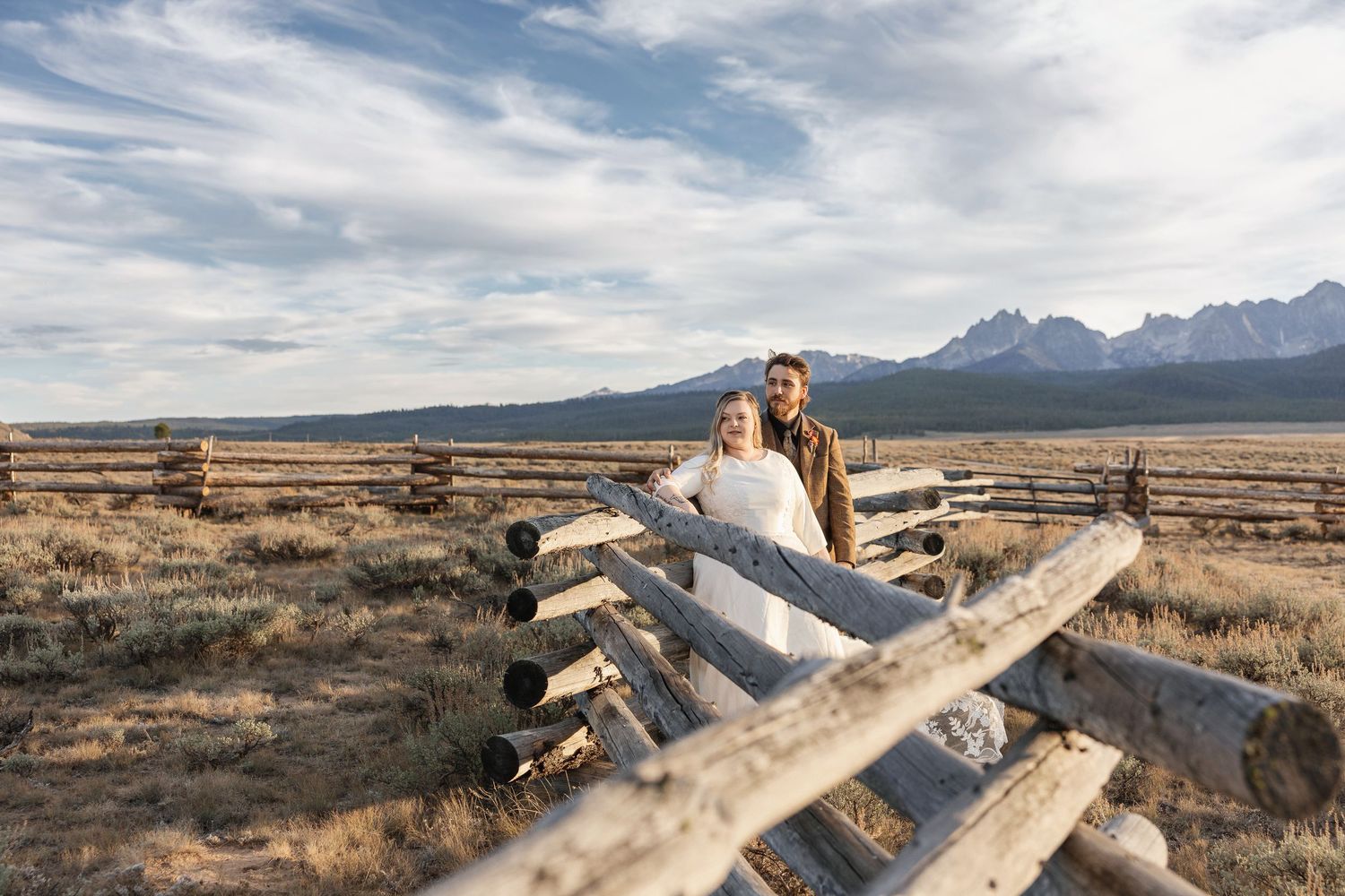 A scenic outdoor wedding ceremony setup with white chairs facing majestic mountain peaks during golden hour.