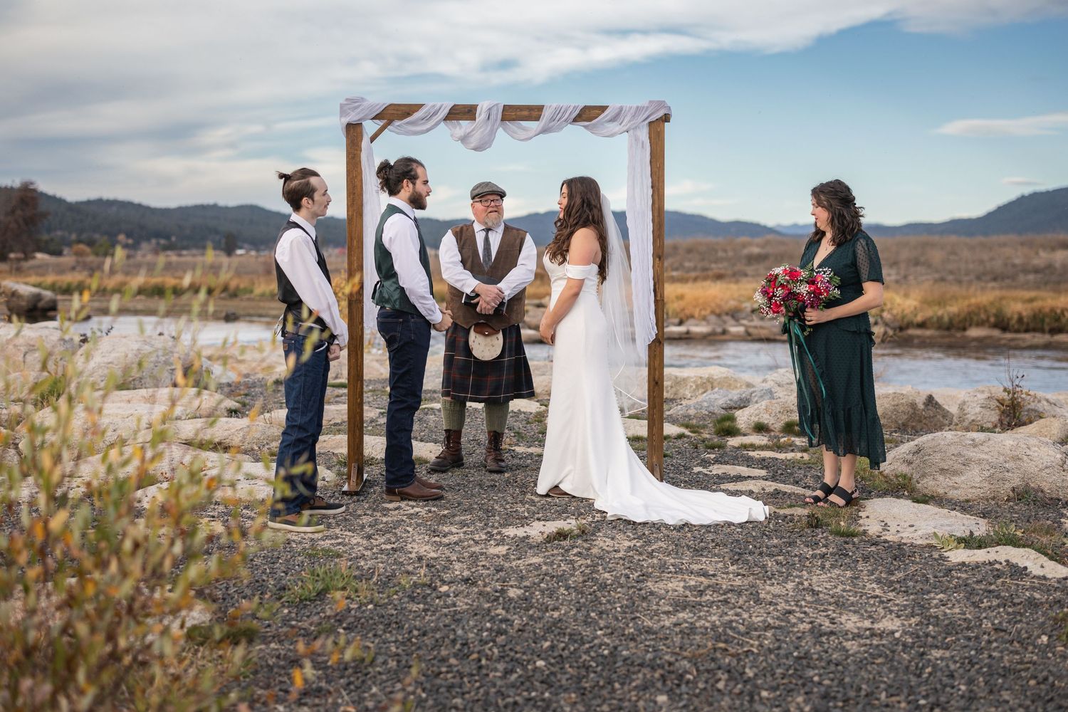 An intimate outdoor wedding ceremony under a simple arch with mountain views in the background.