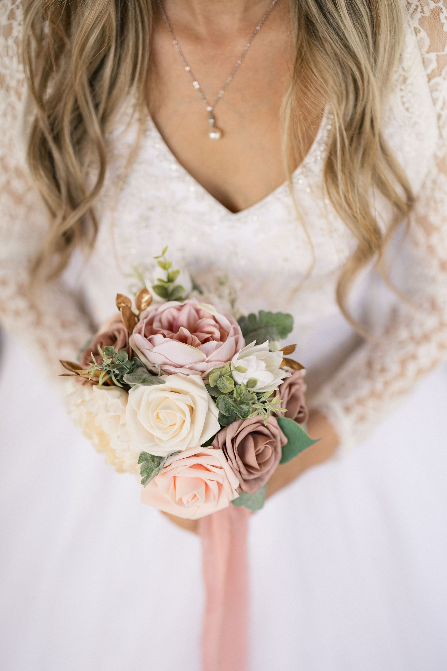 Delicate bouquet of pink and white roses with greenery against lace wedding dress.