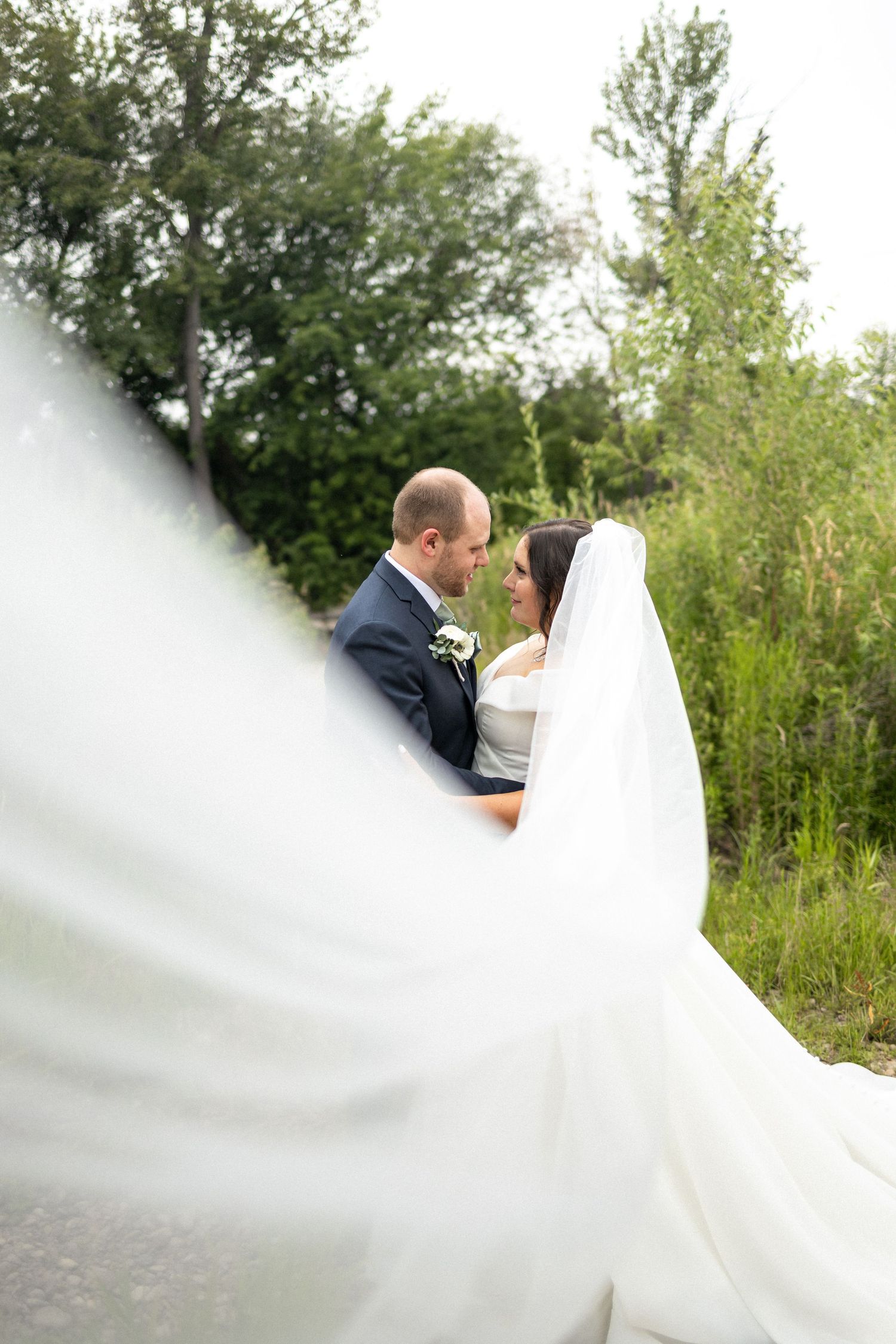 Artistic wedding photo through veil showing couple's intimate moment in nature.