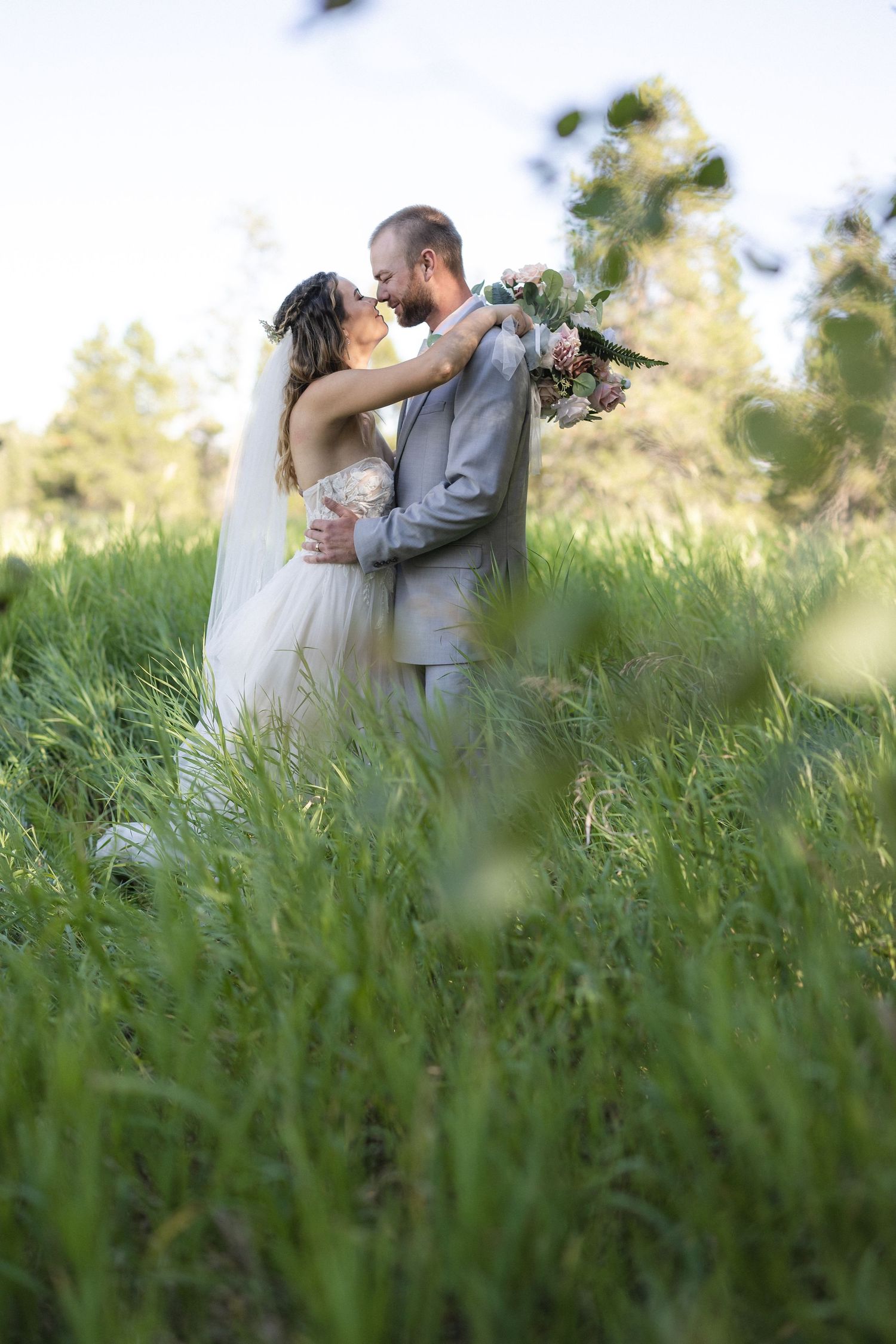 Newlyweds share an intimate moment in tall grass during their outdoor wedding.