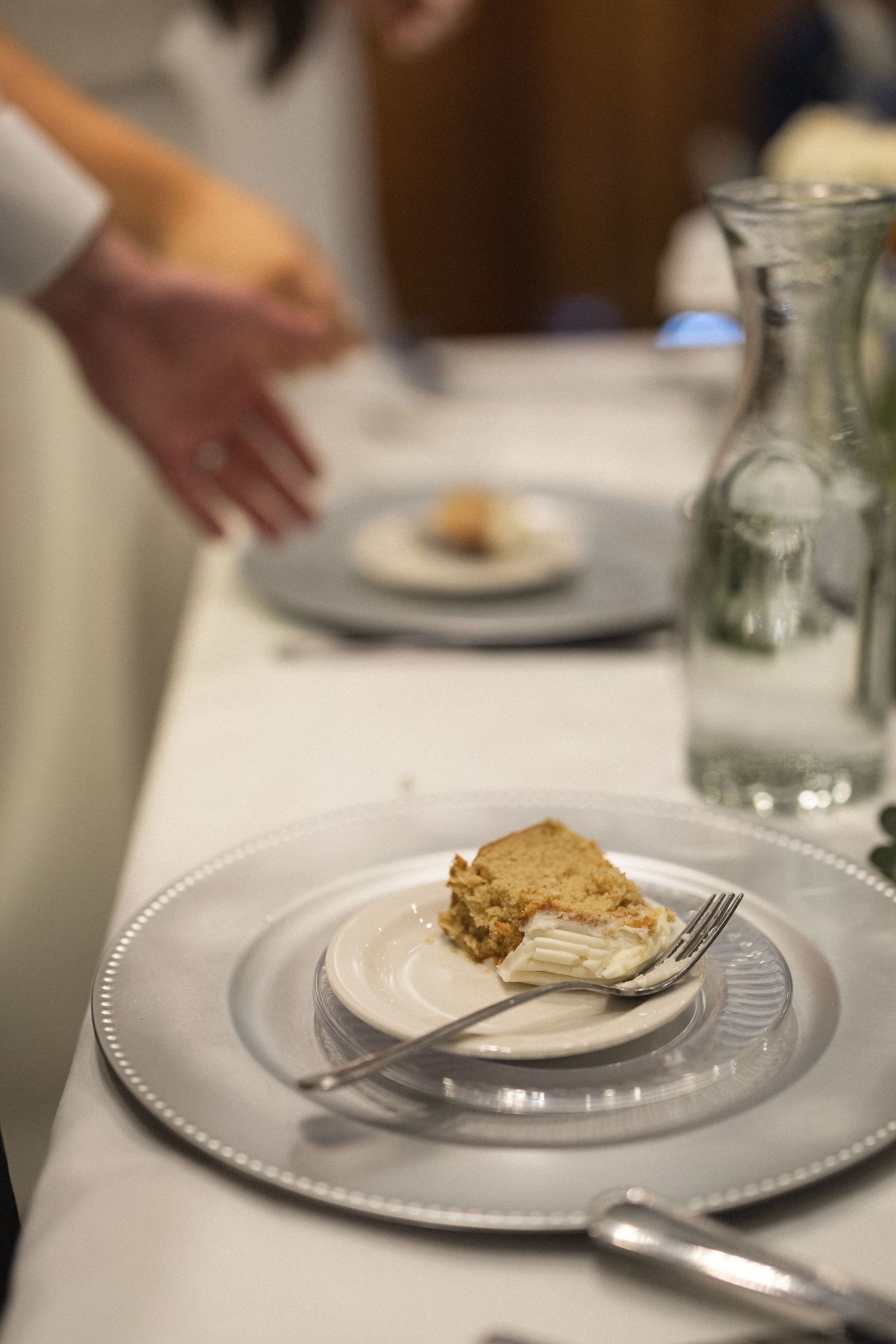 Wedding reception place setting with dessert plate and water glass on white tablecloth.