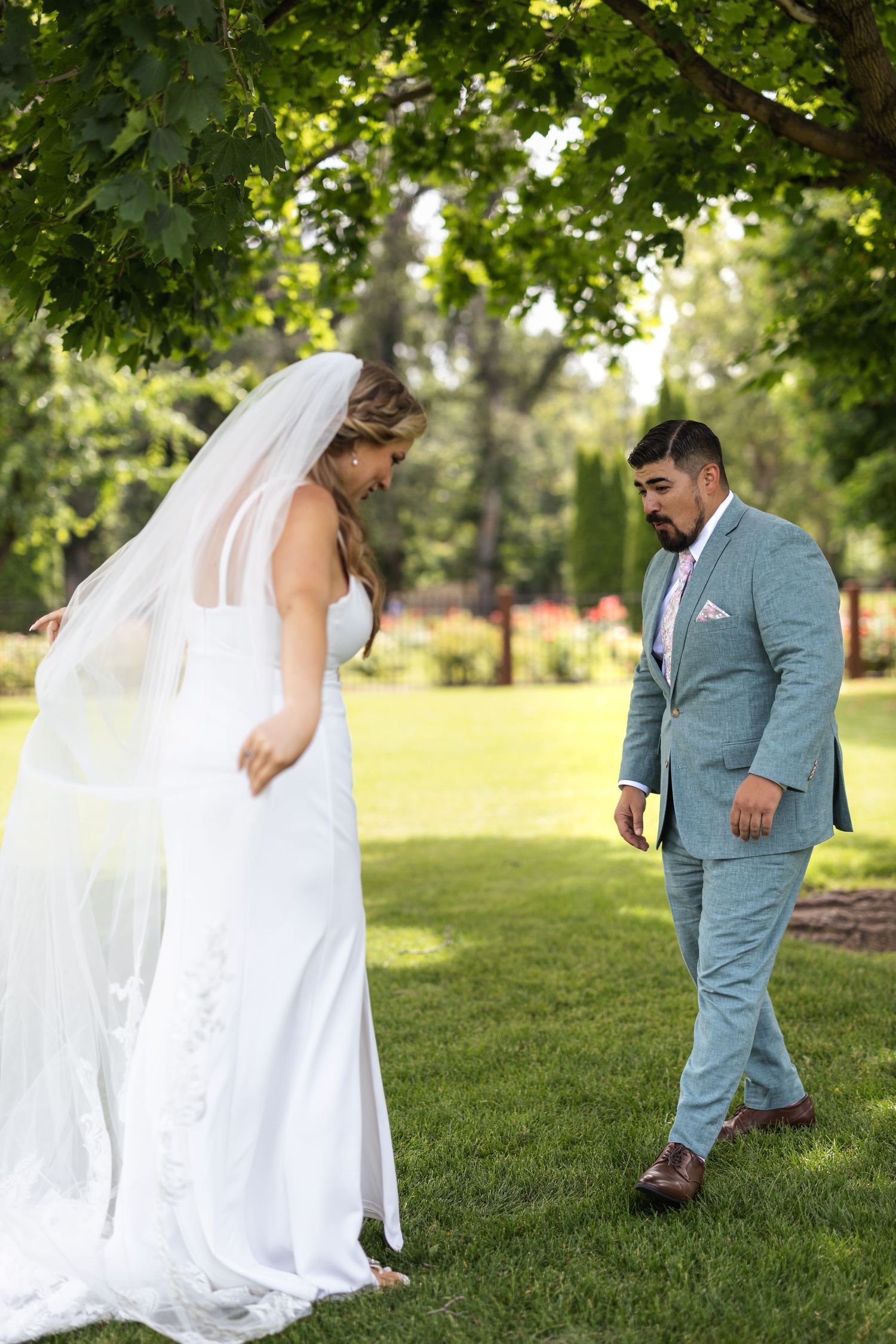 First look wedding moment between couple in white dress and blue suit in garden setting.