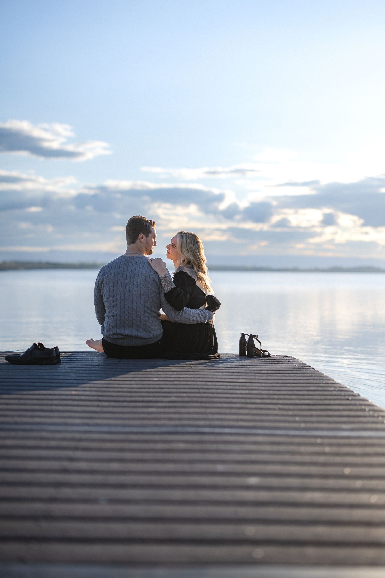 Couple sitting together on dock watching sunset over peaceful lake.