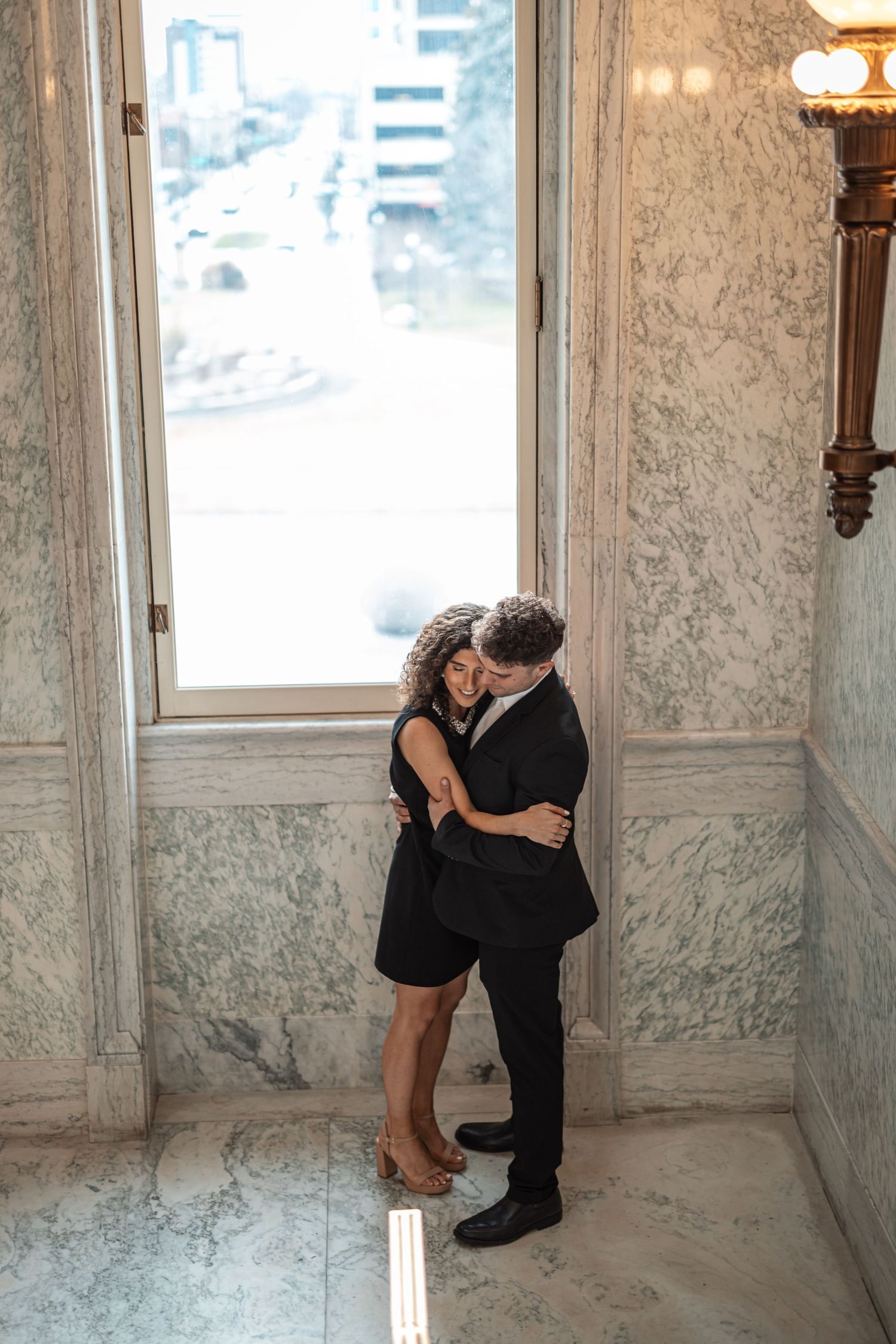 A tender embrace captured in an elegant marble hallway with natural window light.