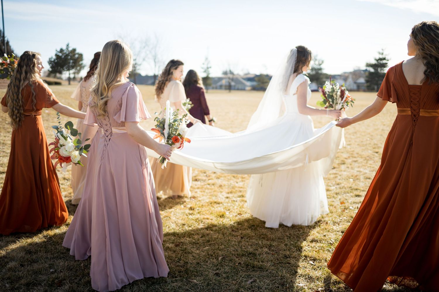 Wedding party in earth-toned dresses poses against golden sunset light.