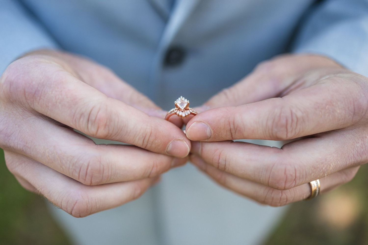 Close up of hands holding a delicate engagement ring with a sparkling diamond solitaire.