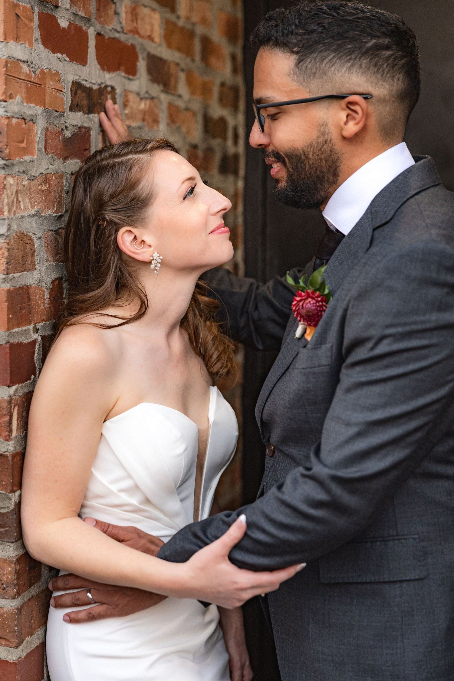 A couple shares an intimate moment against a rustic brick wall.