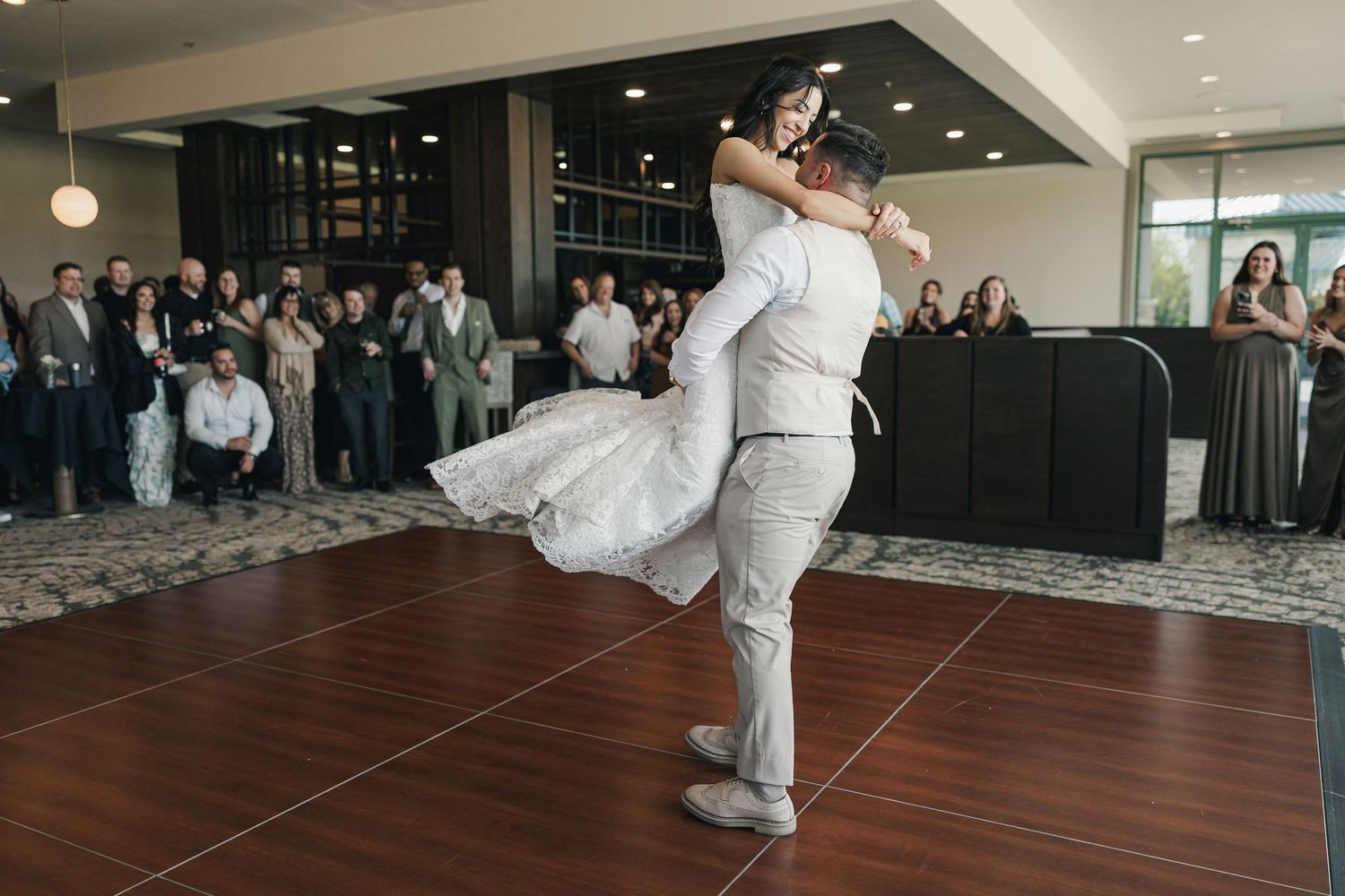 Groom lifting bride in wedding dress during first dance at elegant indoor reception venue.