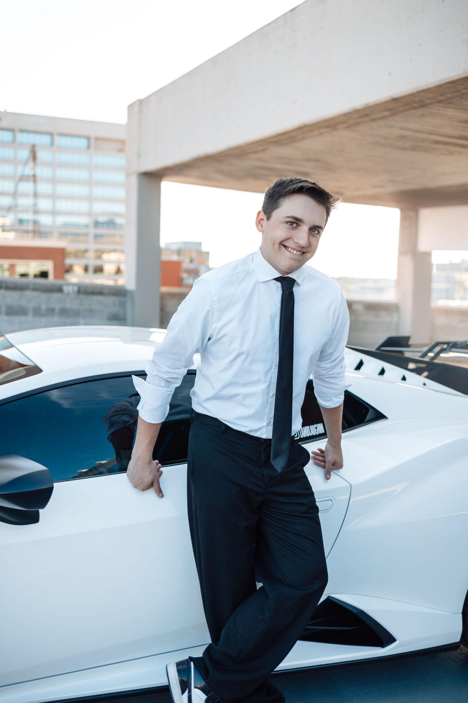 Professional in business attire poses with a sleek white luxury car in a parking garage.