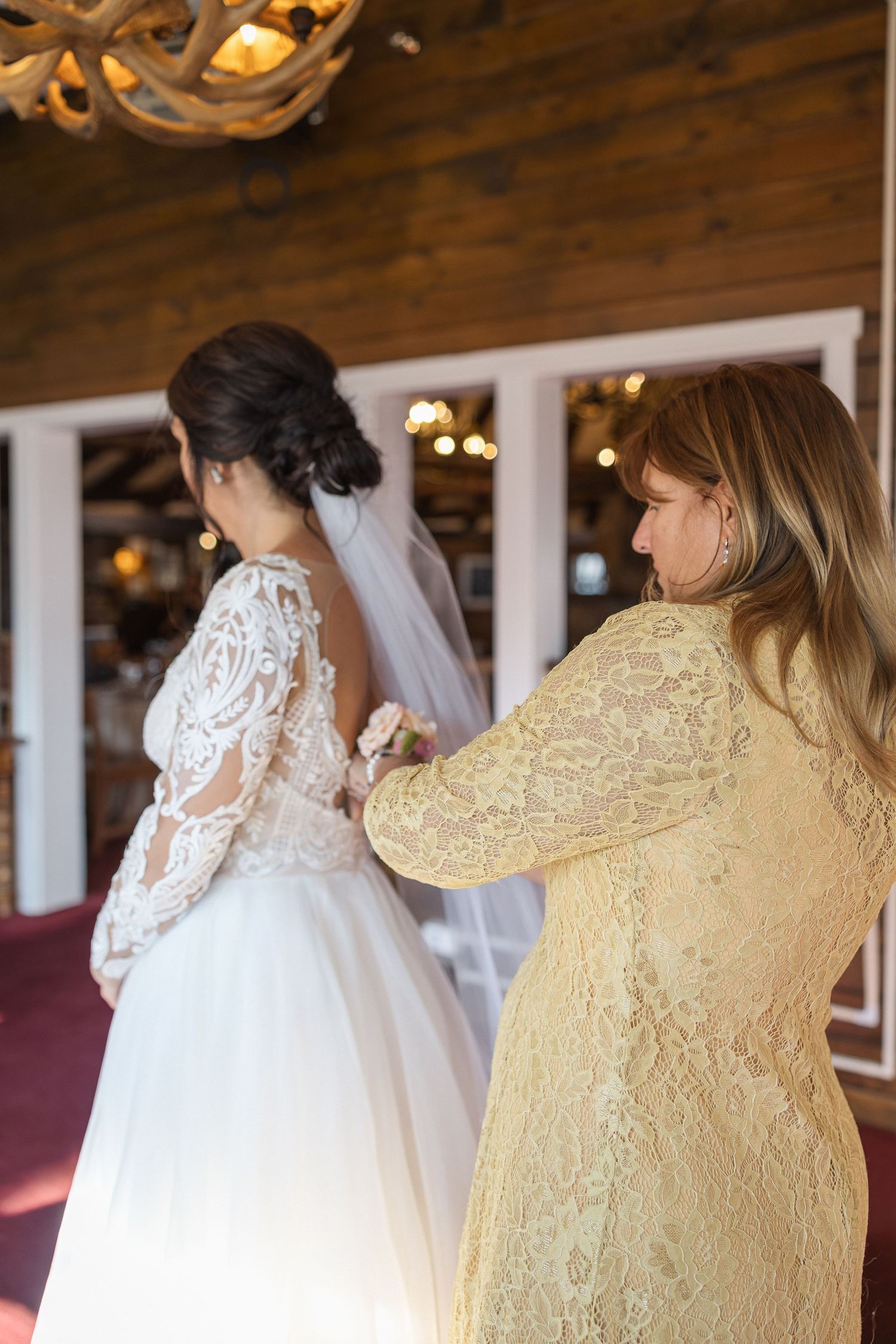 Wedding dress with intricate lace details and yellow dress in rustic wooden interior.