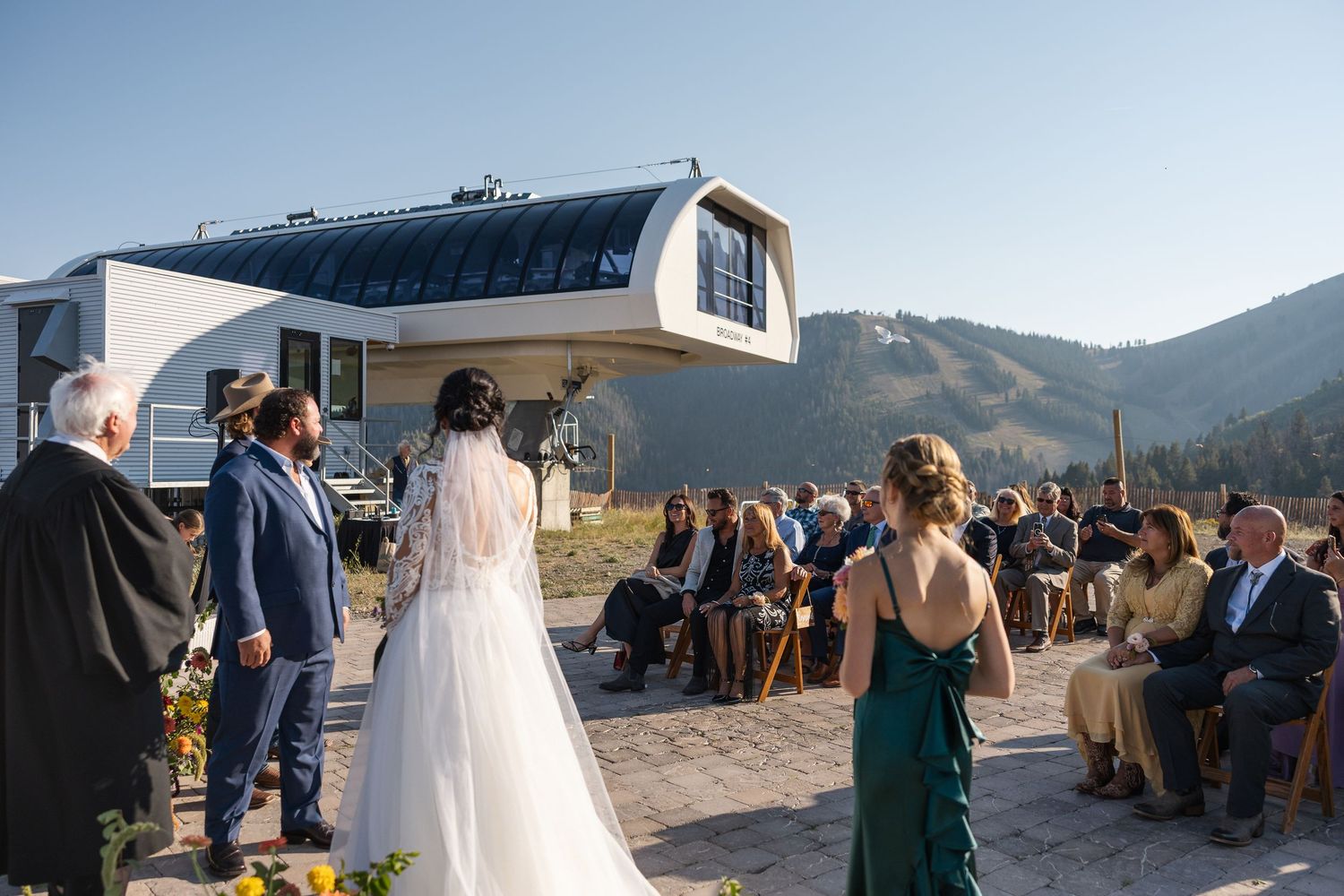 Wedding reception outside mountain lodge with guests seated on patio under blue skies.