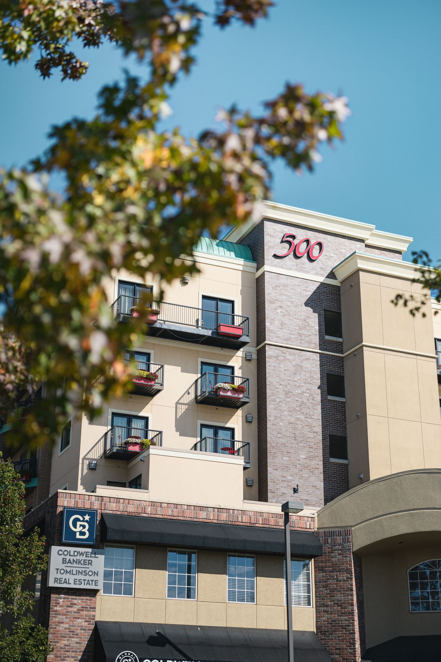 Modern apartment building exterior with balconies and red signage against blue sky.