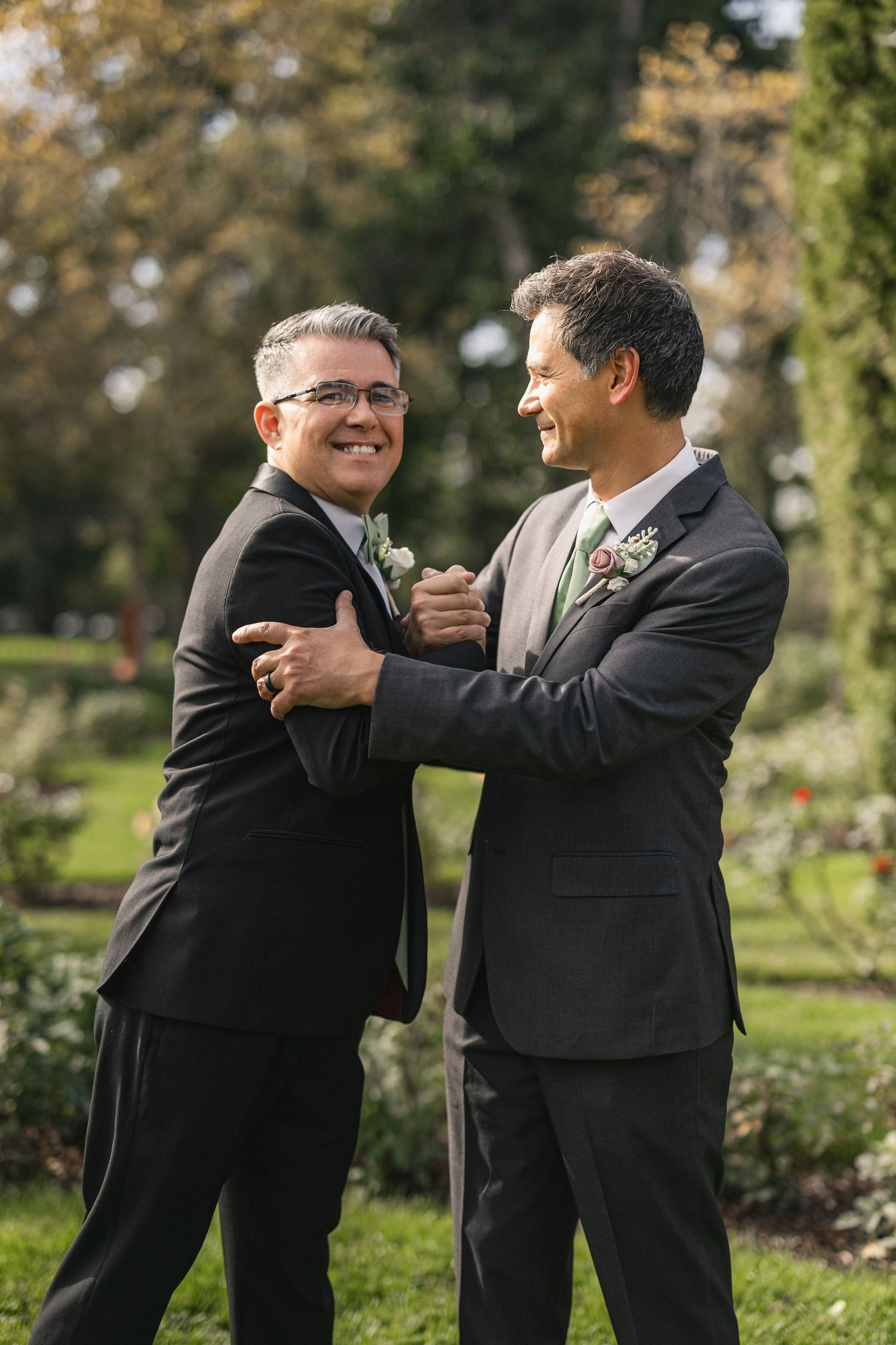 Two men in dark suits share a lighthearted moment during wedding celebrations.