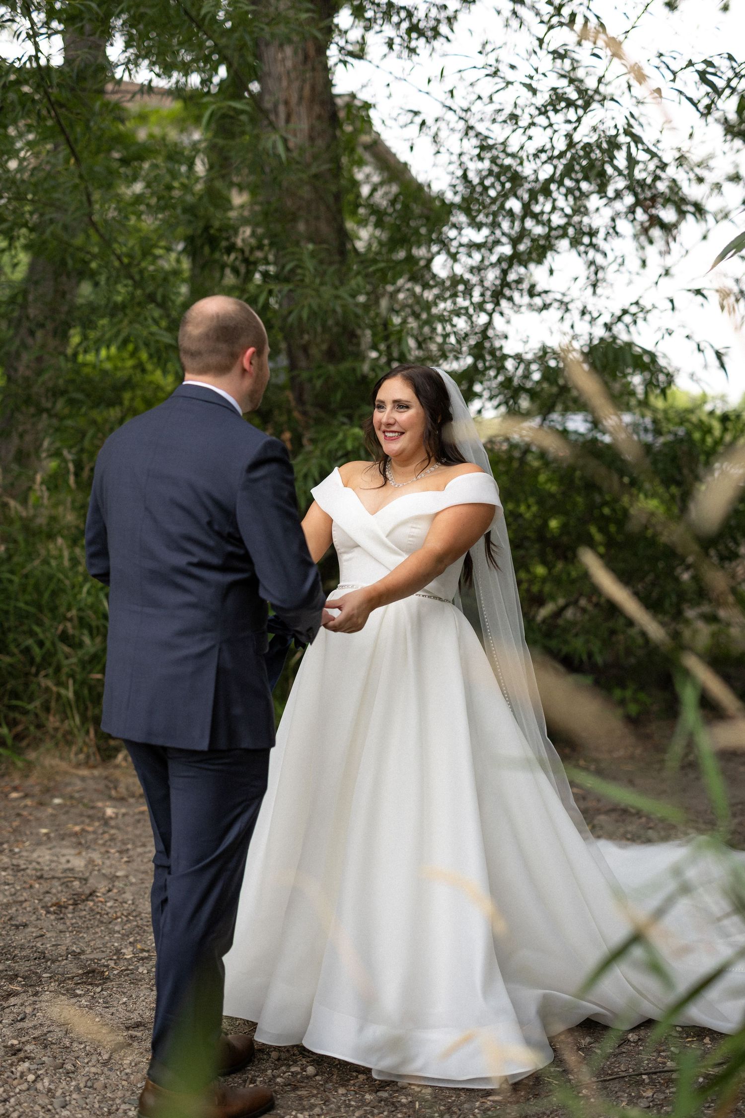 A couple shares an emotional first look moment on a wooded path during their wedding day.