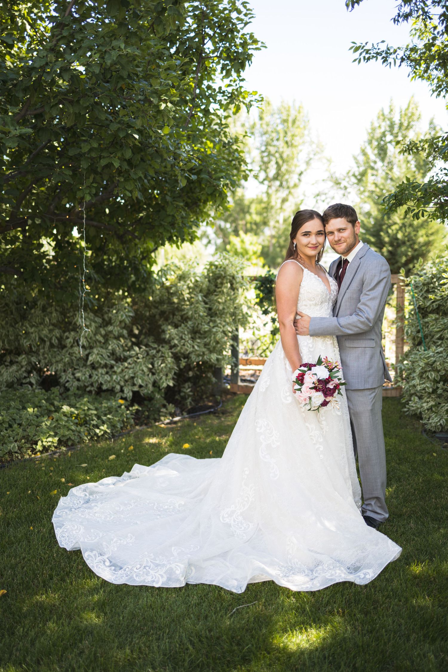 A wedding portrait in a lush garden setting with flowing white dress and grey suit.