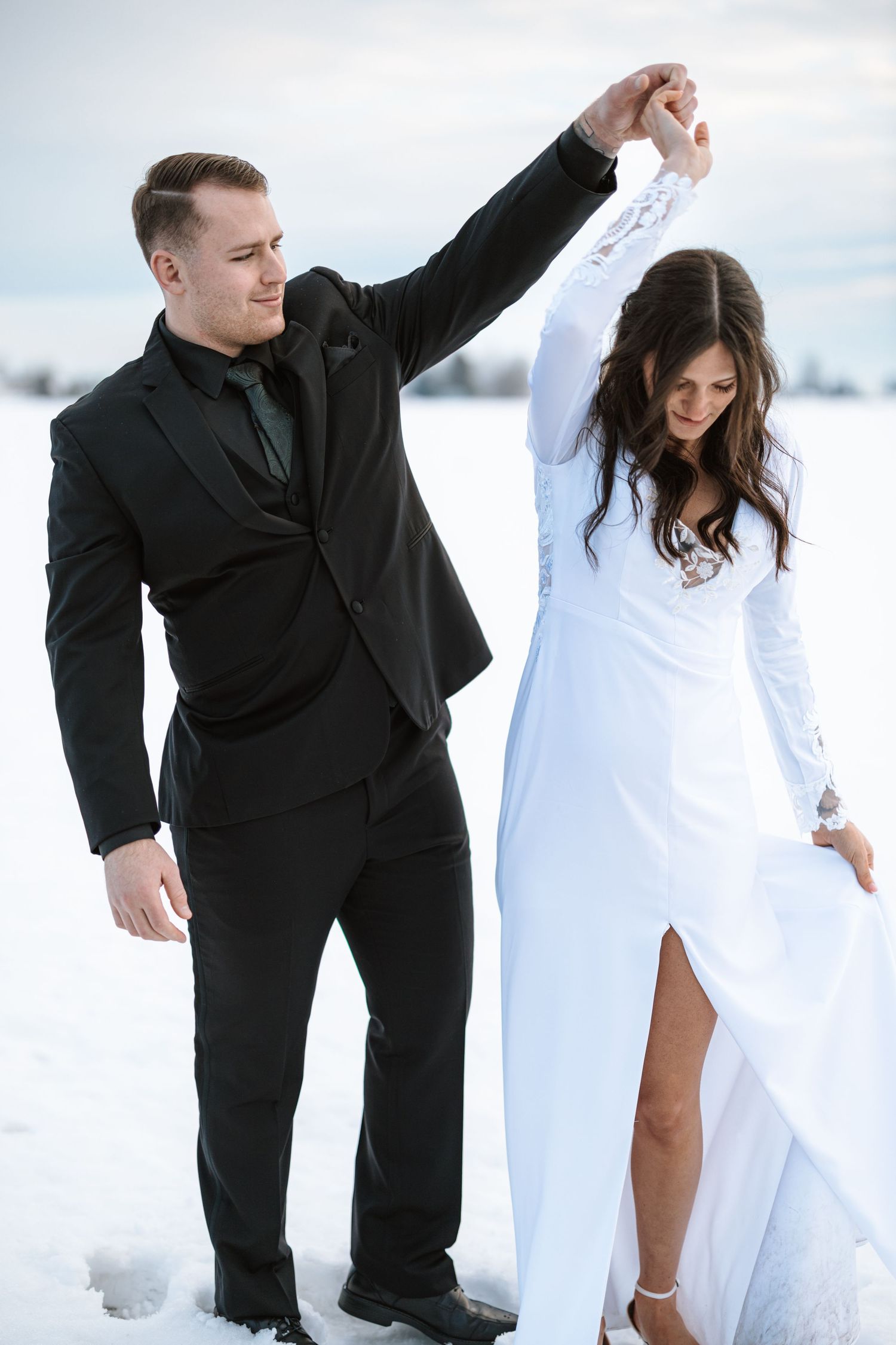 Couple dances in formal attire against snowy winter backdrop.