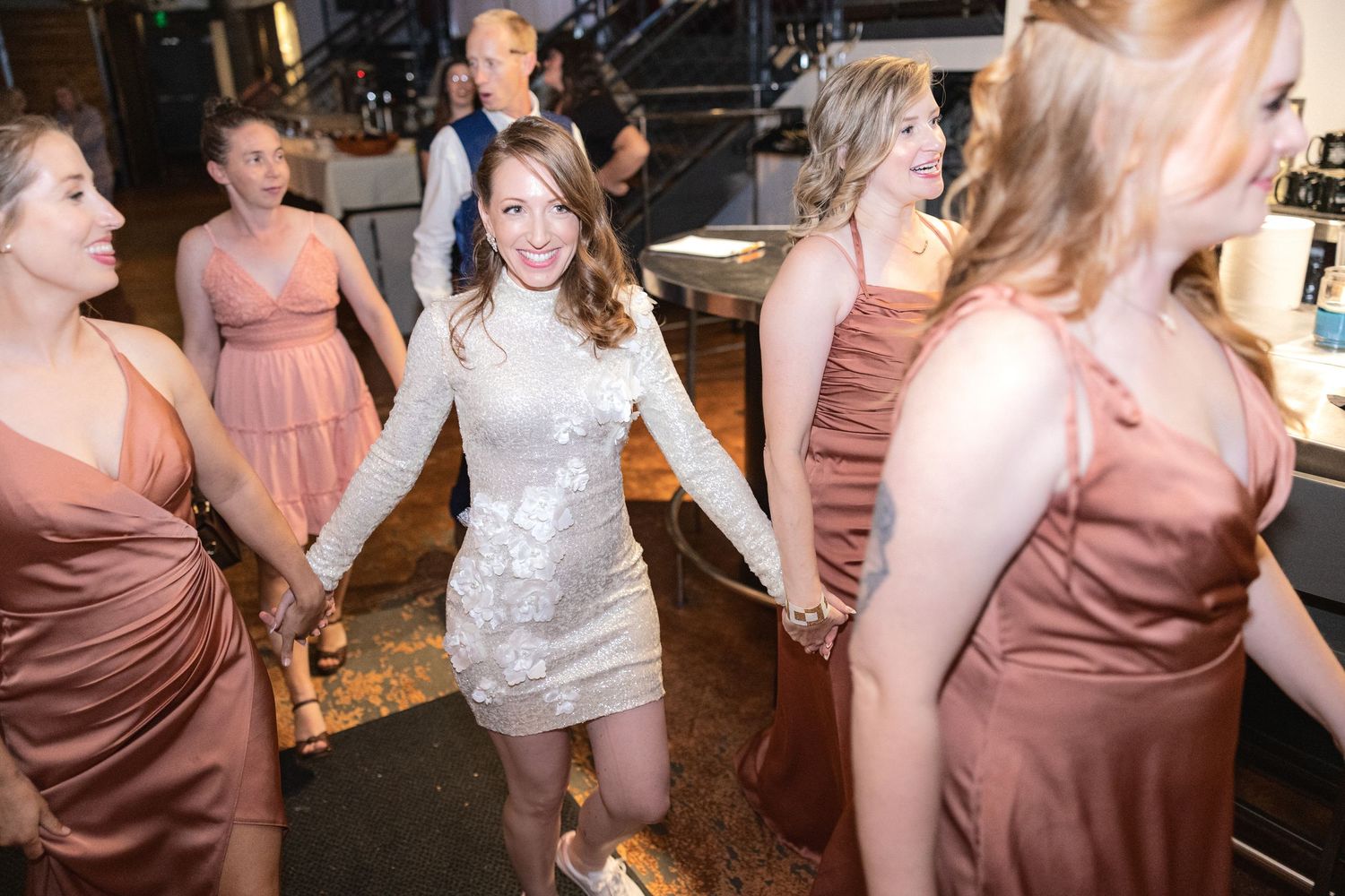 Wedding party guests dancing in mauve bridesmaid dresses at an indoor reception venue.