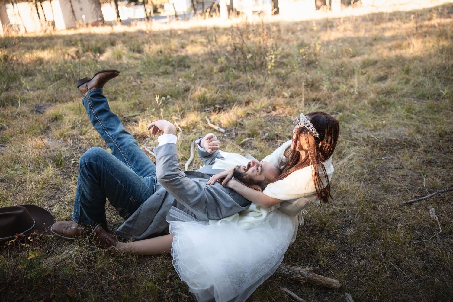 Wedding couple creates dynamic poses on the ground during a forest photoshoot at sunset.