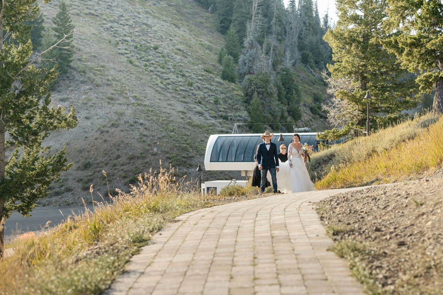 Wedding party walks along a stone pathway with mountain scenery and a ski lift in the background.