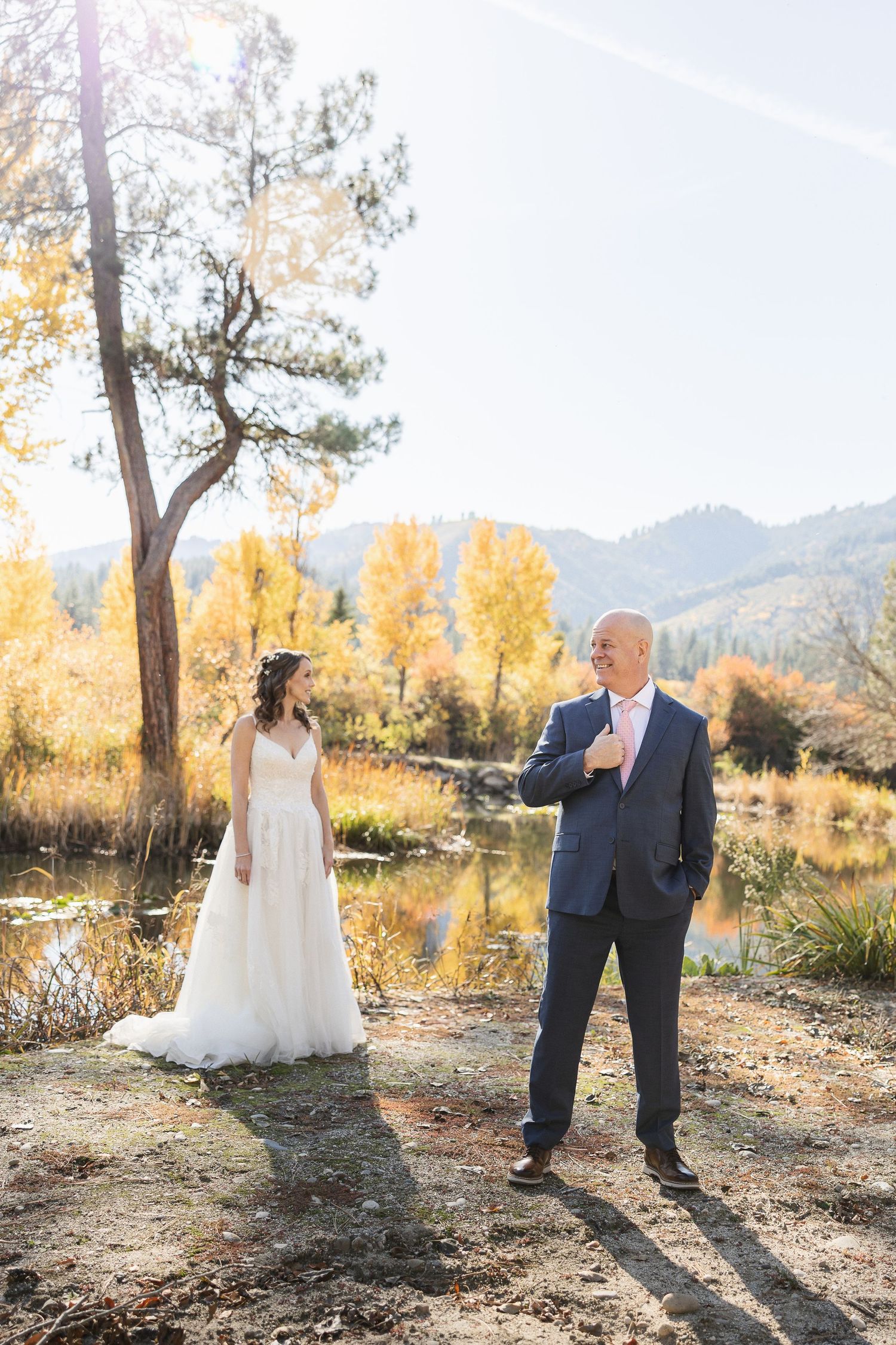 A wedding couple poses in an autumn landscape with golden trees and mountains in the background.
