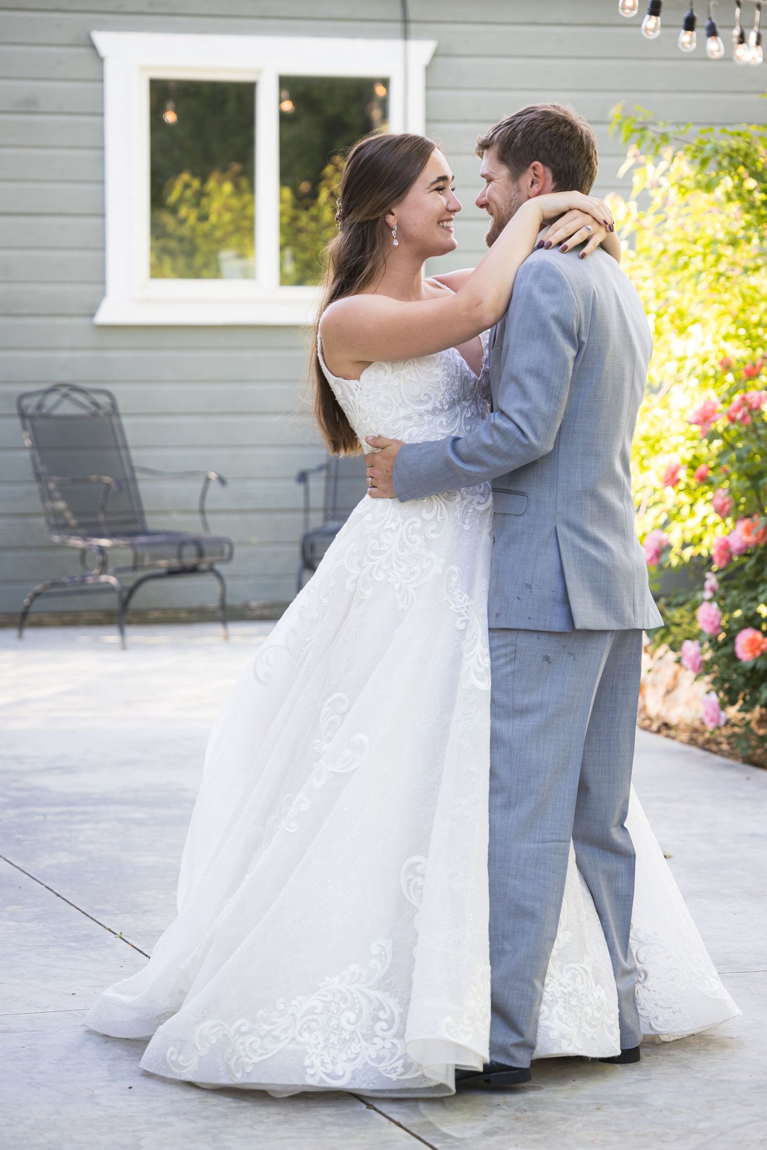 A couple embraces on a patio during their wedding celebration with string lights overhead.
