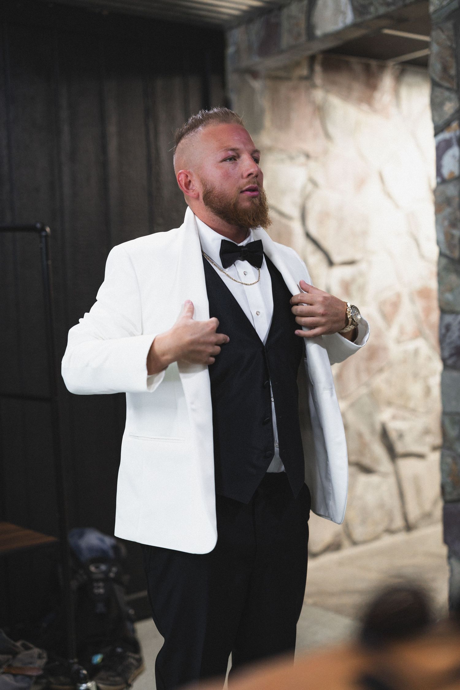 Groom in classic white dinner jacket adjusts his bow tie.