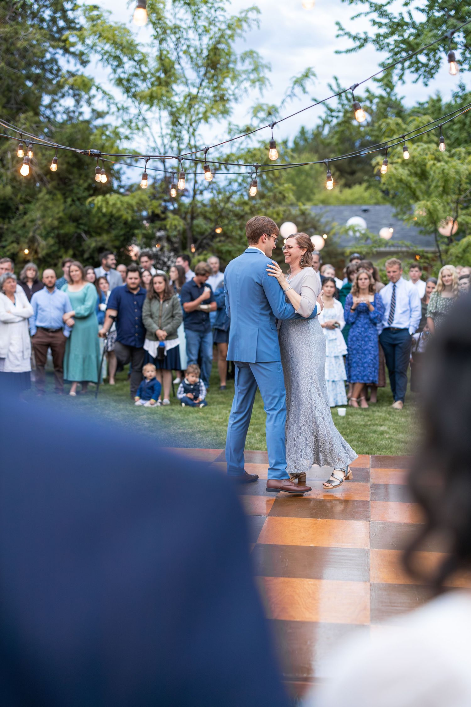 Romantic first dance at an outdoor wedding with string lights and gathered guests.
