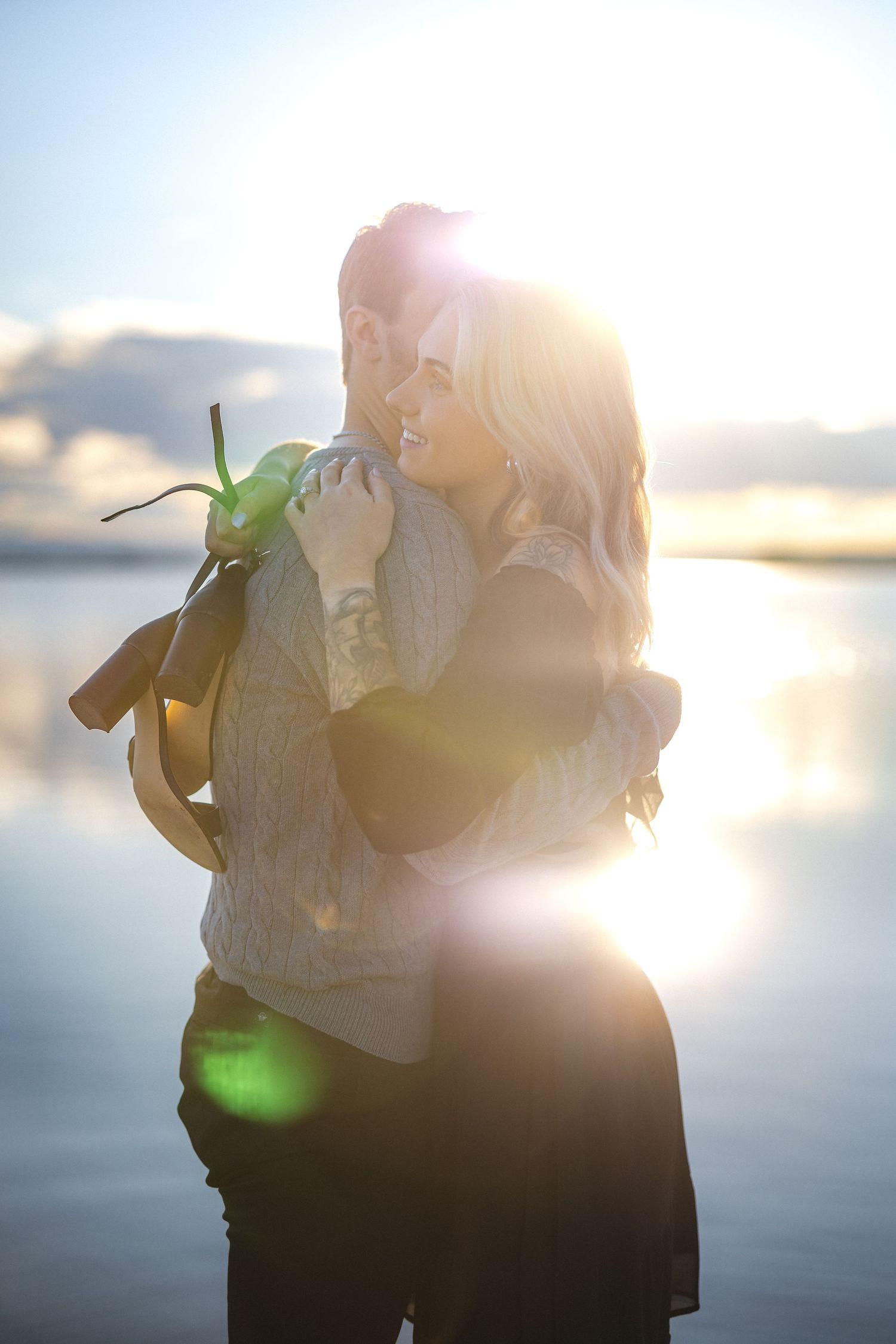 A couple embraces in backlit sunset glow on a waterfront dock.