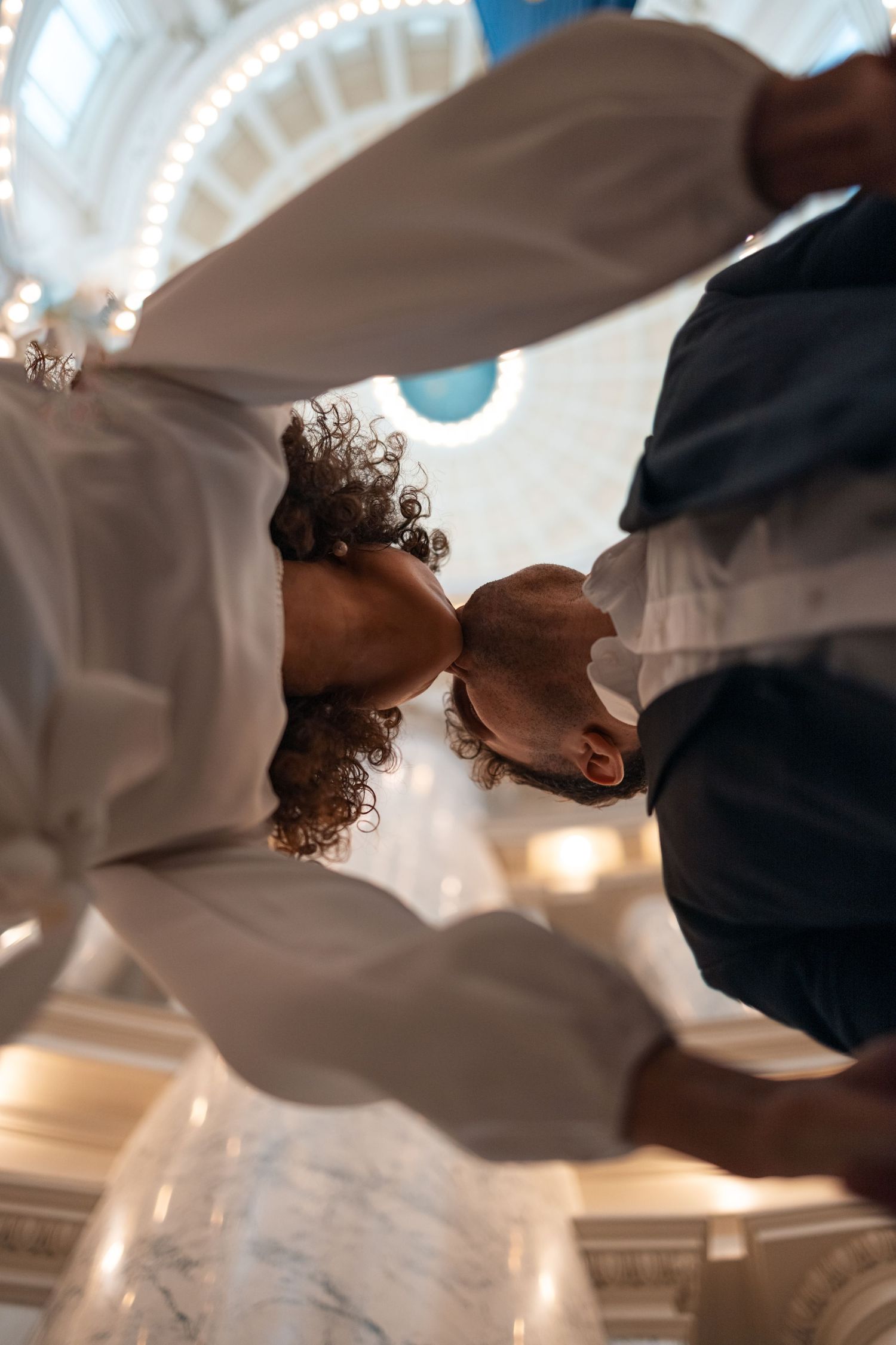 Low angle view of couple kissing under ornate domed ceiling with decorative lighting.