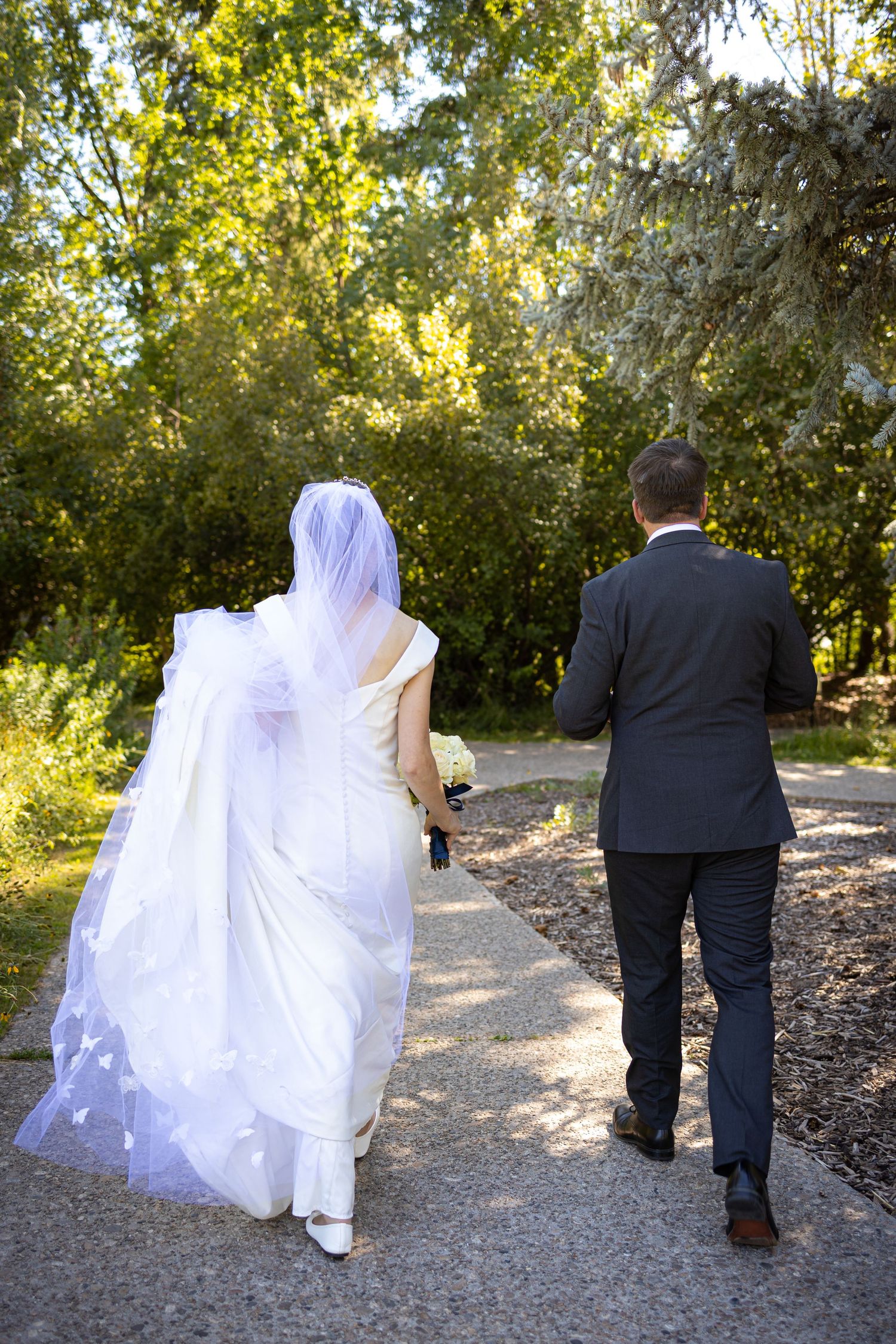 A couple walks down a tree-lined path after their wedding ceremony.