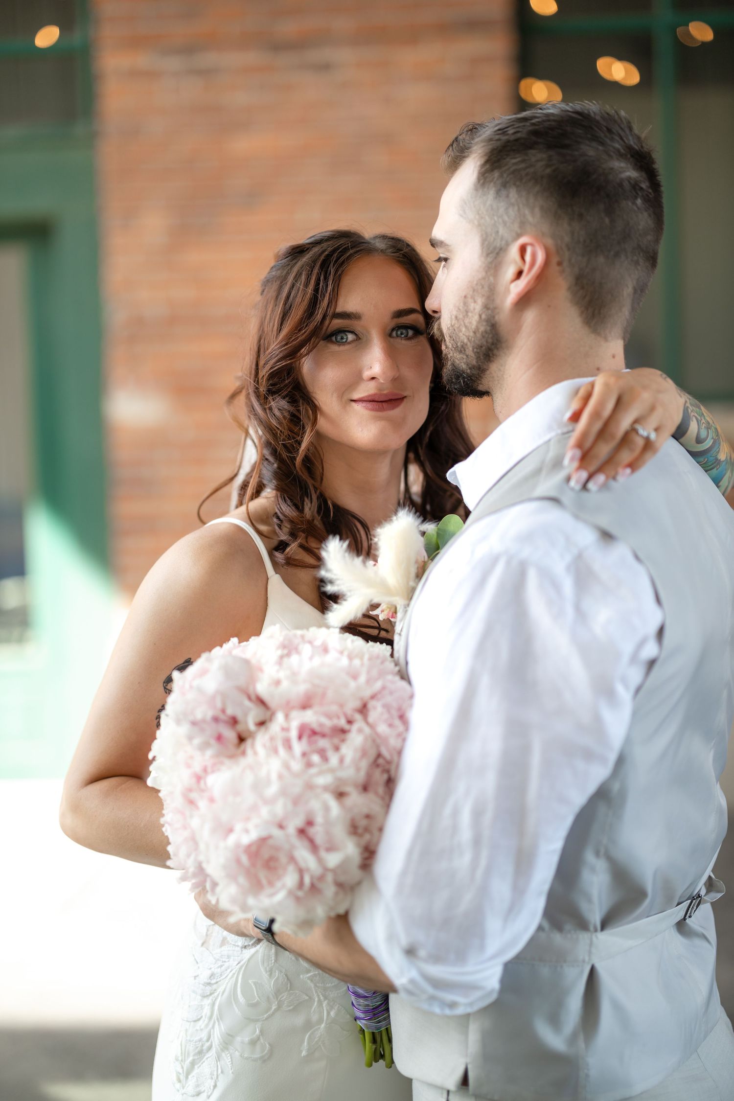 Intimate wedding portrait with the bride holding a pink bouquet against a brick backdrop.