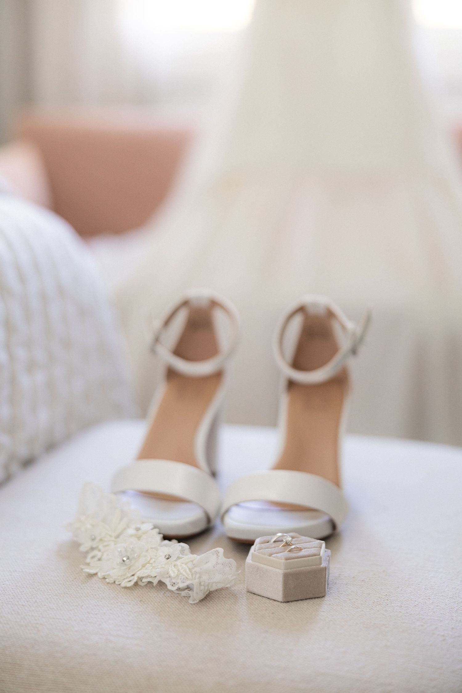 White bridal shoes with delicate lace details displayed on white bedding.