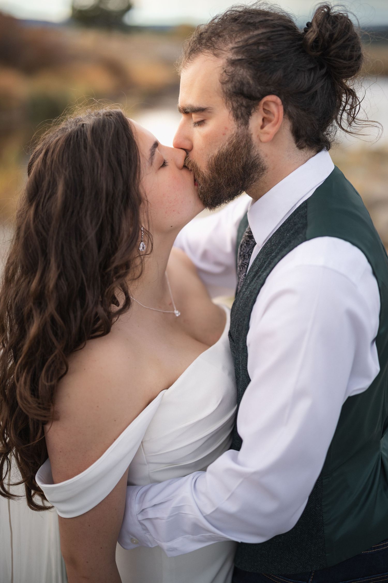 Intimate wedding portrait of a couple kissing, with the bride in white and groom in vest and formal attire.