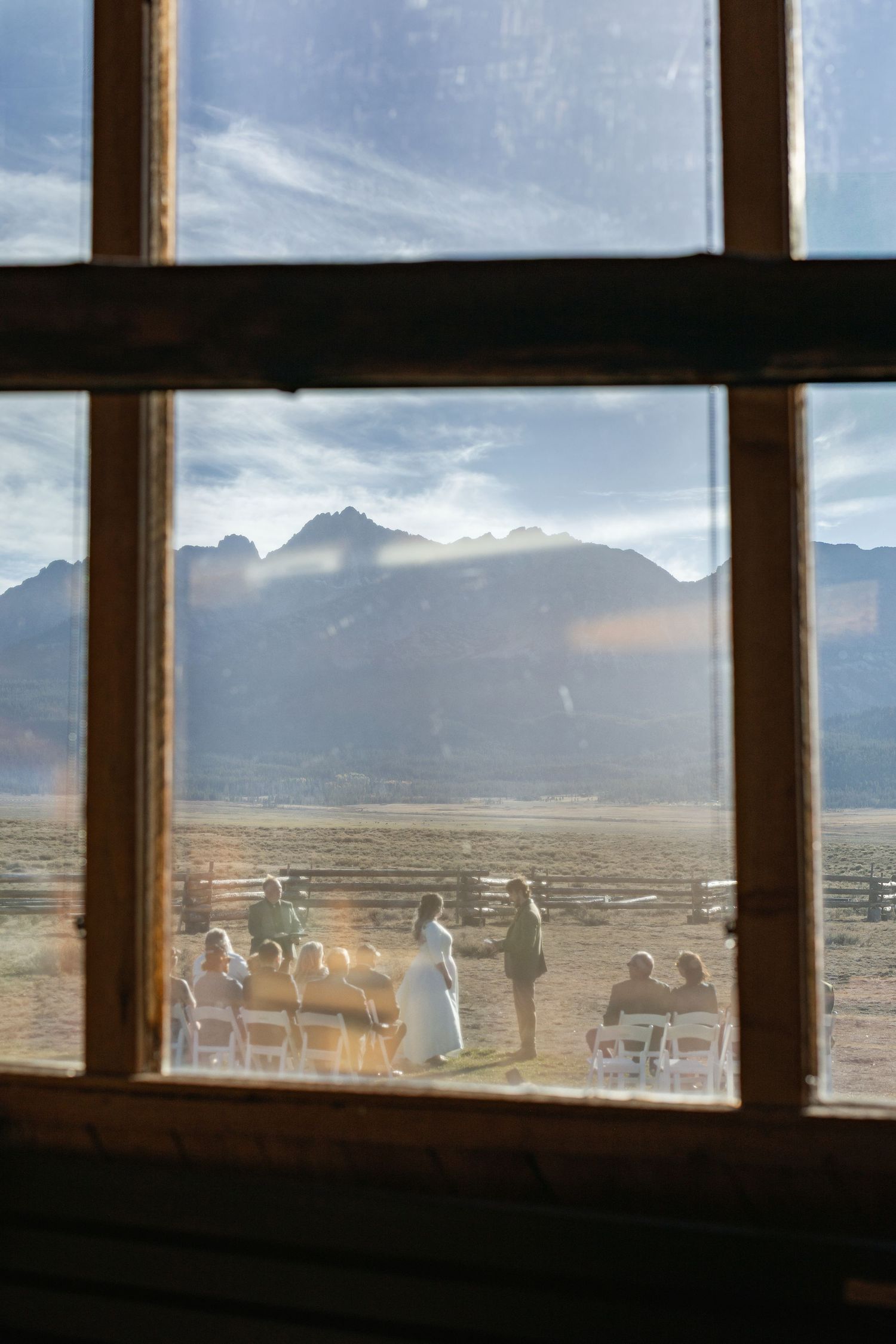 Panoramic mountain landscape viewed through multiple window panes with silhouettes of people gathering outside.