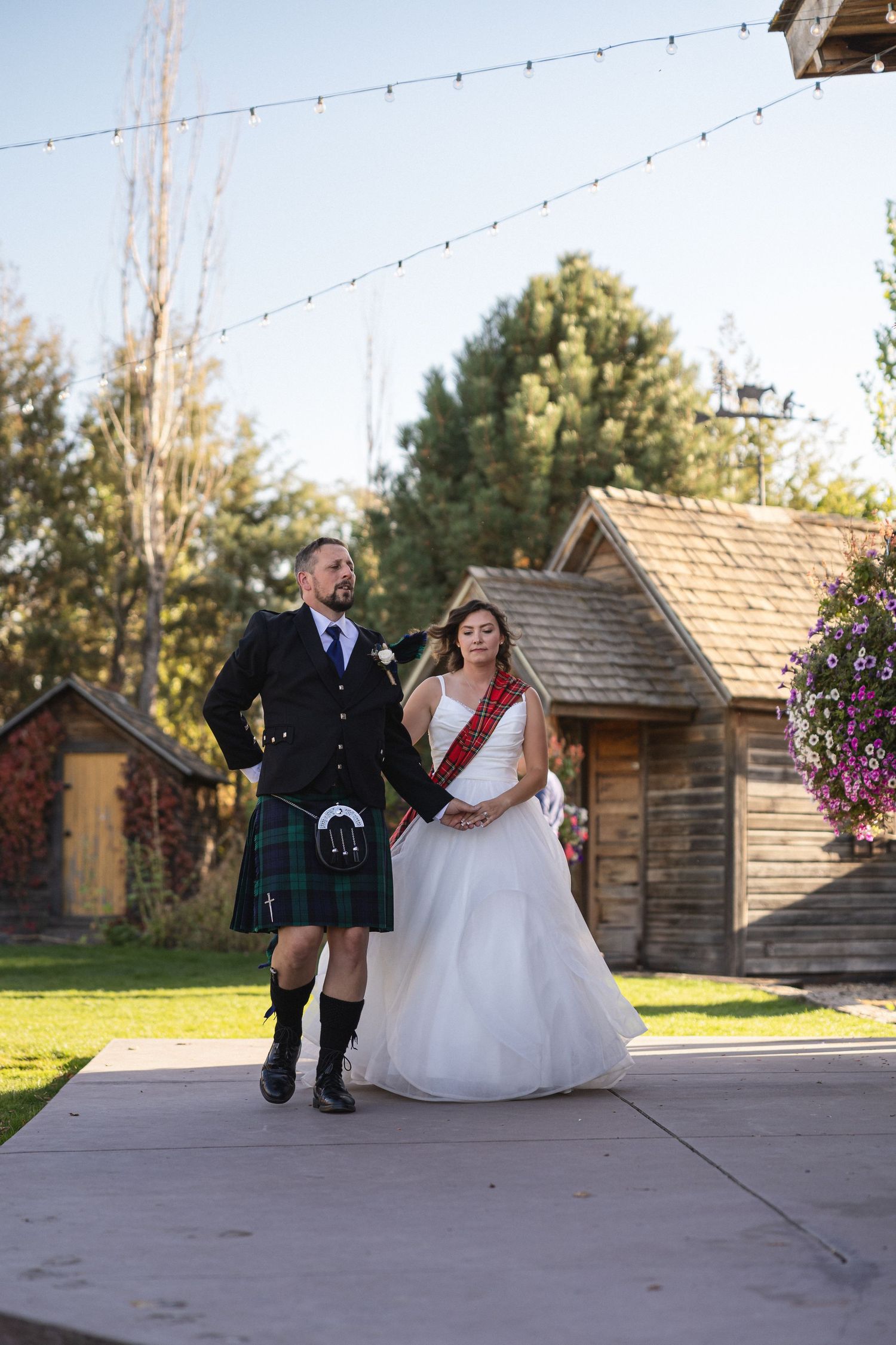 Couple in wedding attire with groom wearing traditional Scottish kilt standing outdoors.