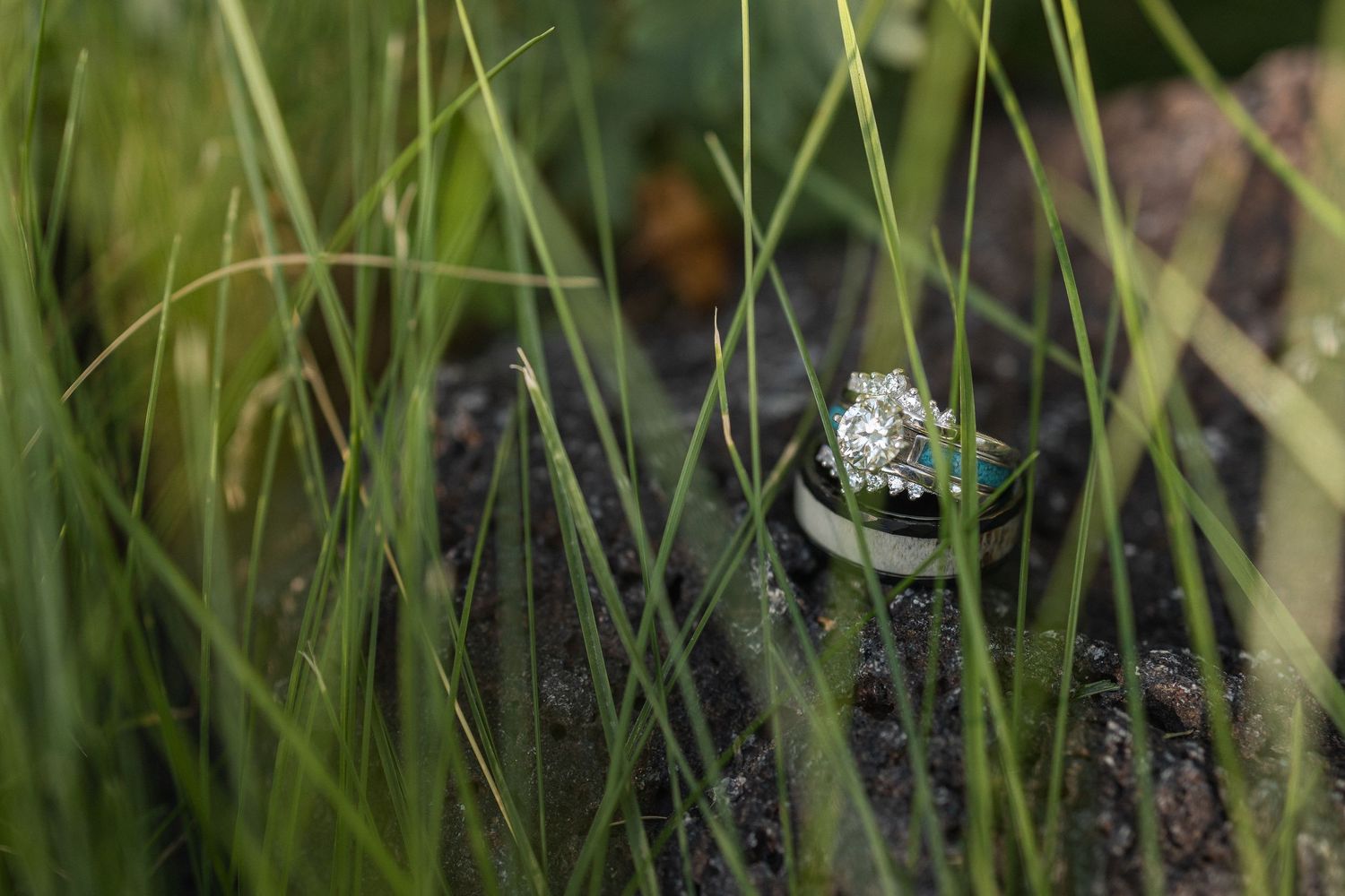 A close-up macro photograph of a tiny water droplet on green grass blades in nature.