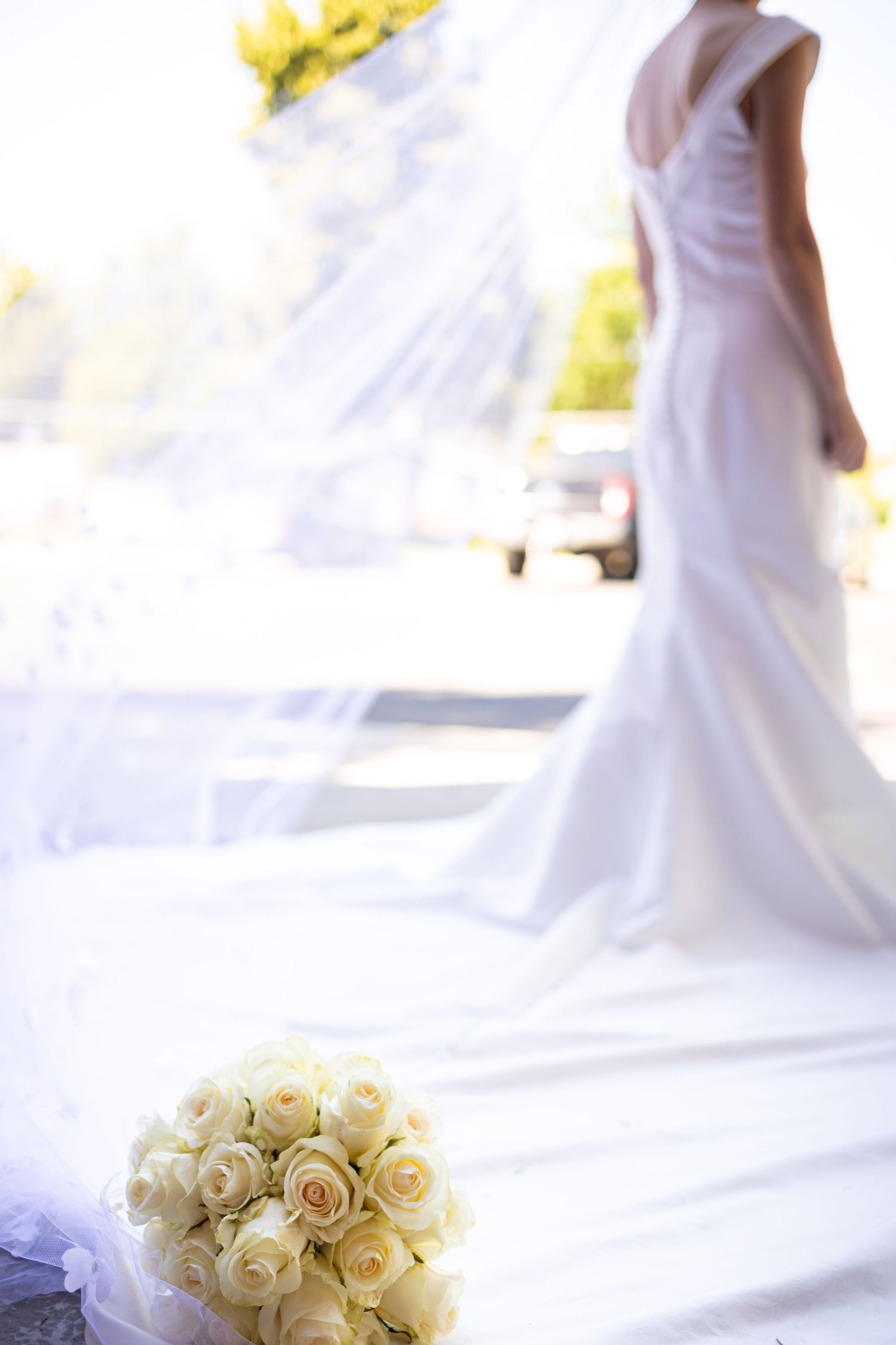 Dreamy backlit silhouette of bride in flowing dress with white rose bouquet in foreground.
